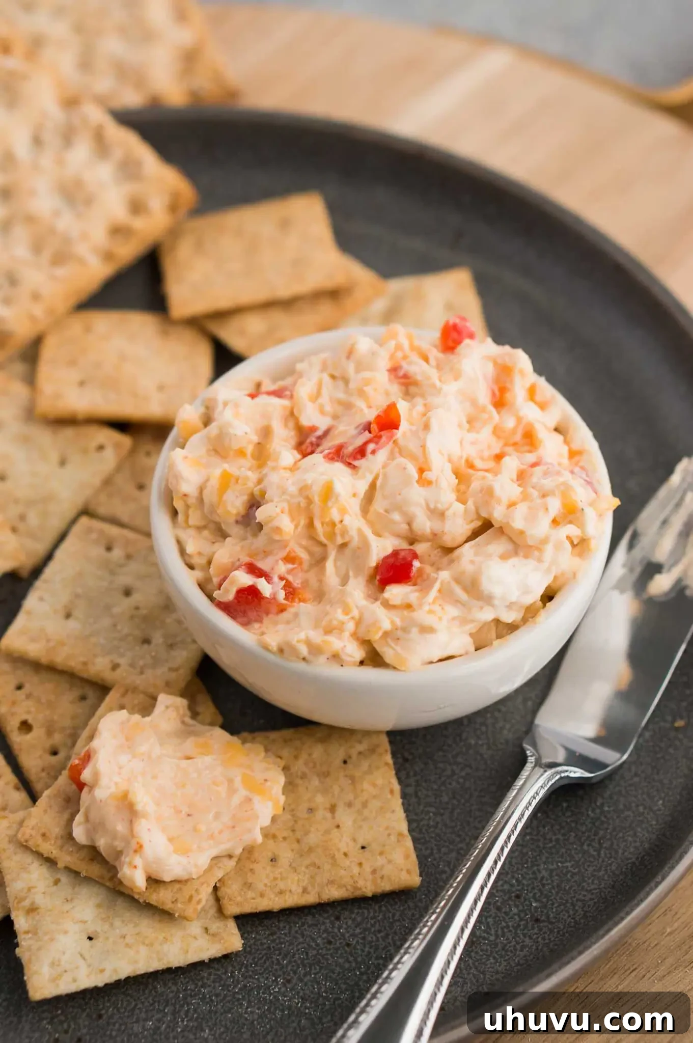 Close up image of pimento cheese dip in a bowl with crackers on a plate, highlighting its creamy texture.