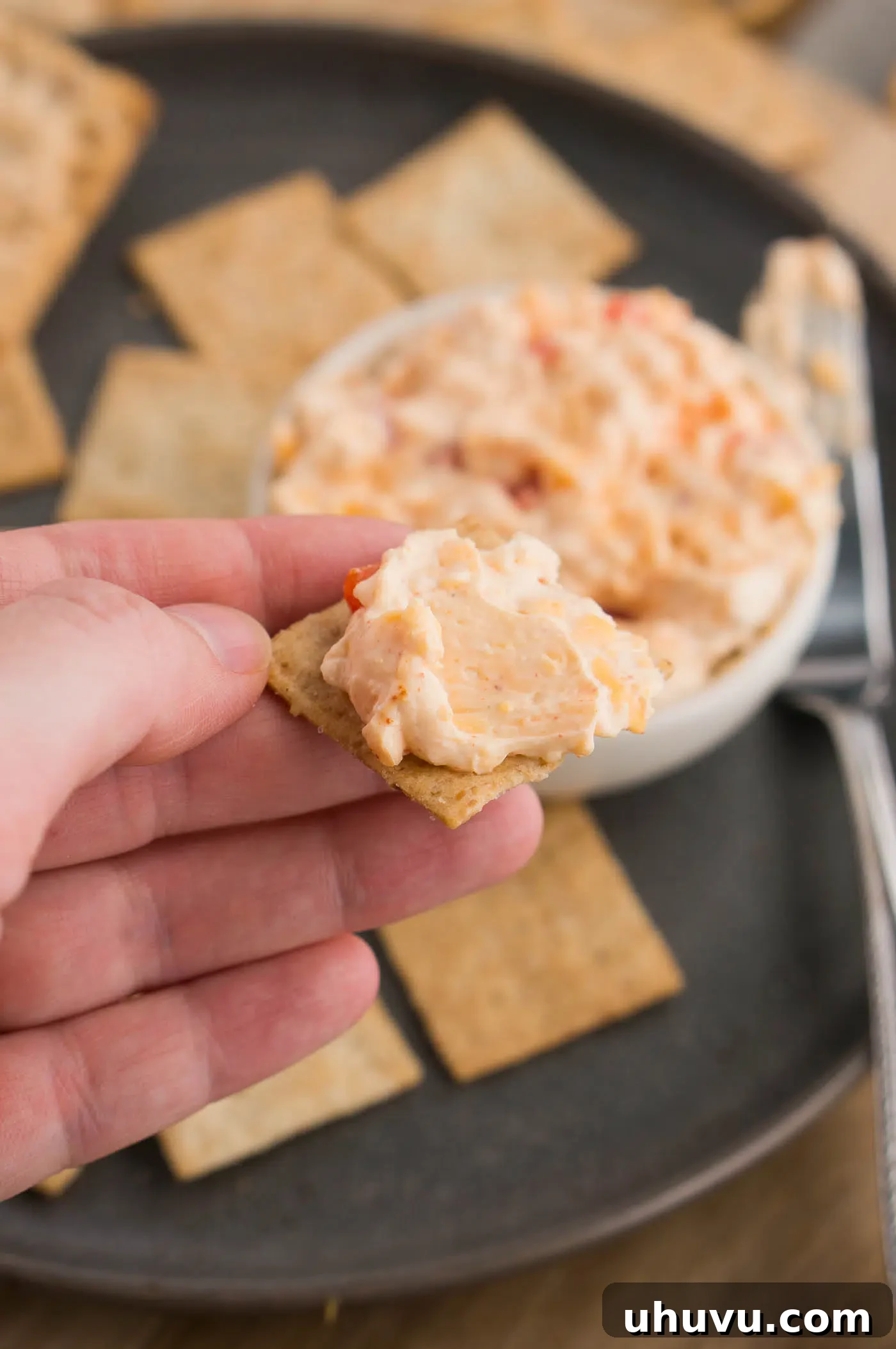 A cracker generously topped with a dollop of homemade pimento cheese spread, ready to eat.