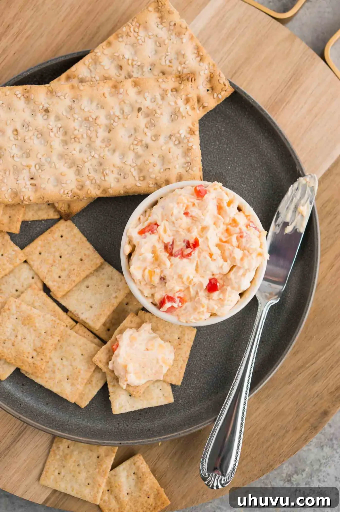 Overhead view of a bowl of pimento spread with crackers arranged on a plate next to it.