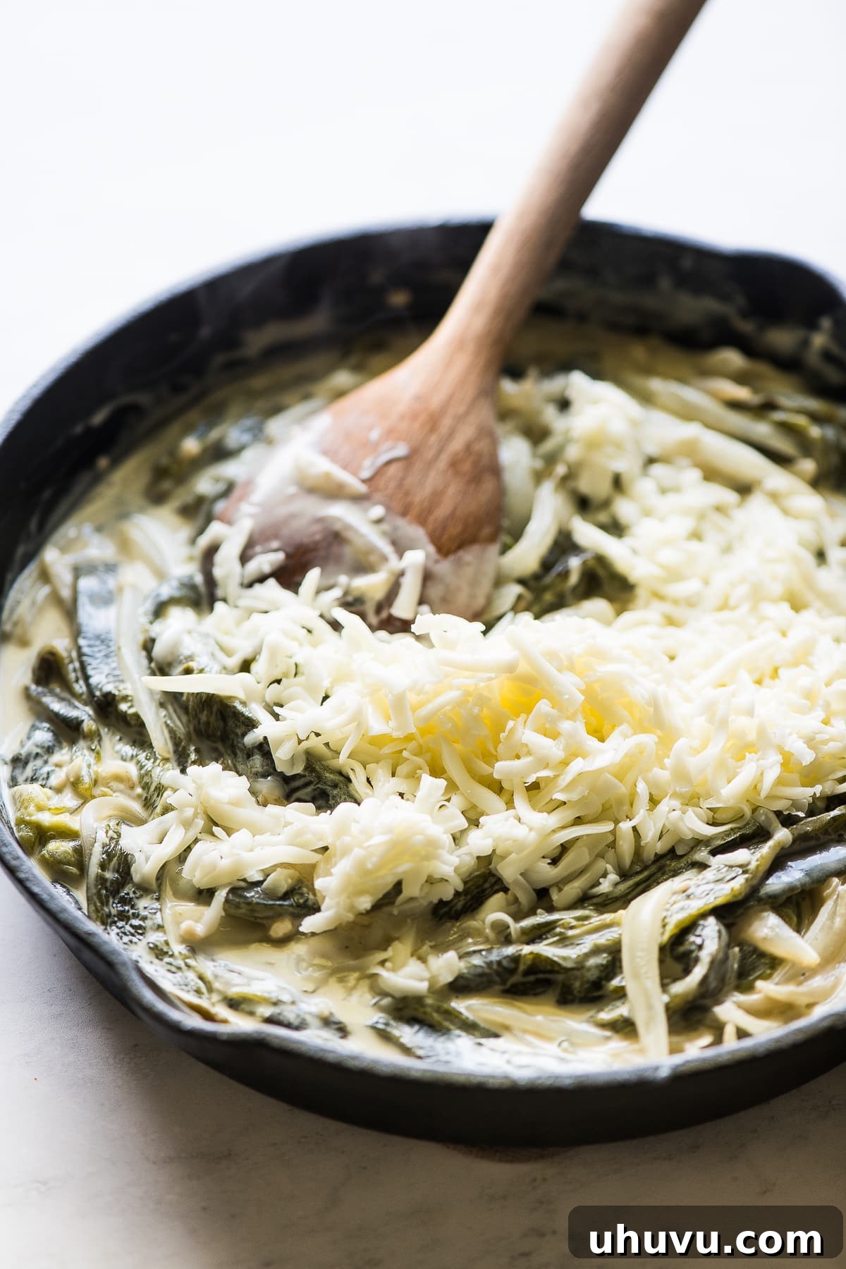 Shredded Oaxaca cheese being stirred into the creamy rajas con crema mixture in a skillet, melting to create a smooth sauce.