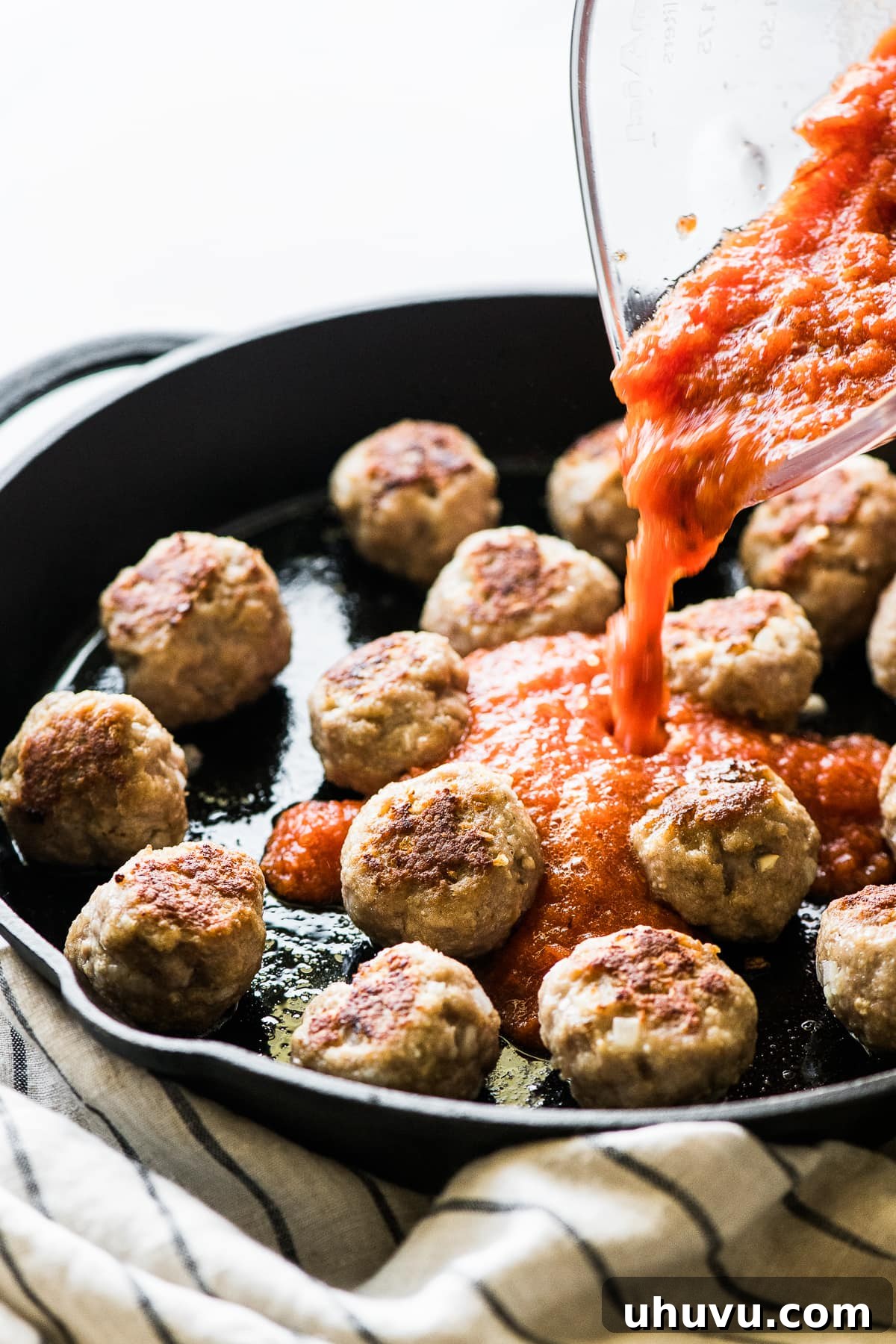 Spicy Albondigas 8 Smoky chipotle tomato sauce being poured over browned Mexican meatballs in a cast iron skillet.