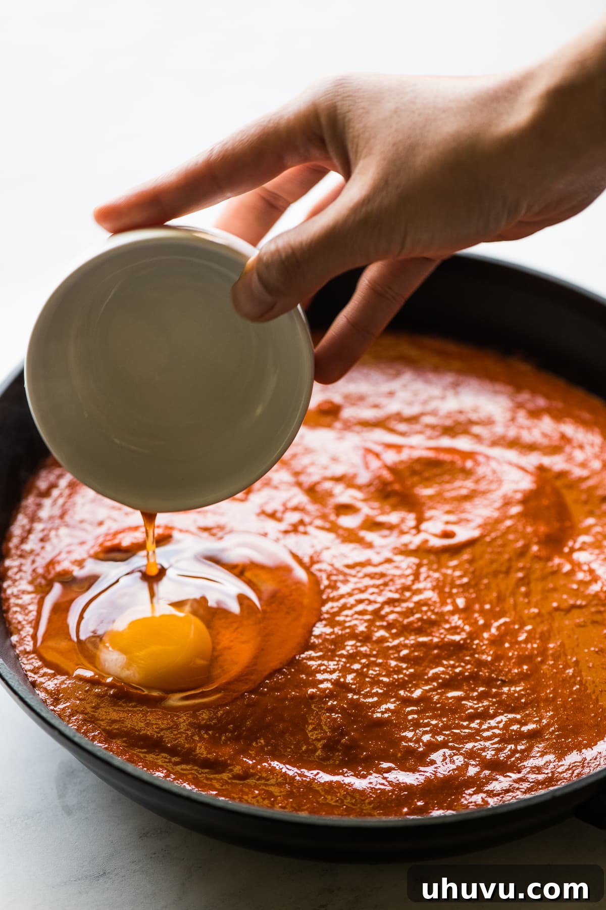 Salsa-Poached Eggs 10 An egg being poured into a skillet with salsa for huevos ahogados.