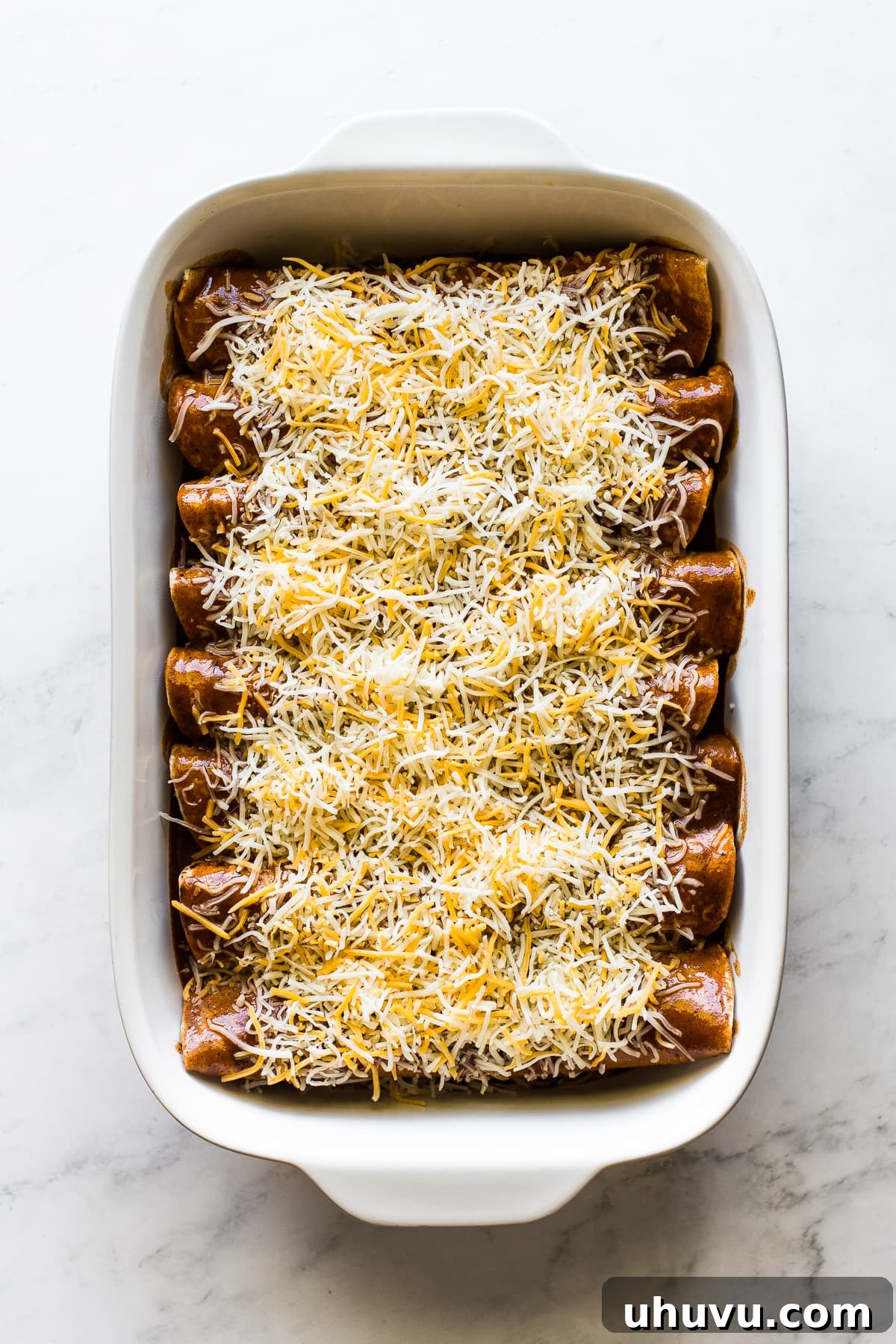 Hearty Beef Enchilada Fiesta 6 Enchiladas ready to be baked in a pan topped with enchilada sauce and shredded cheese.
