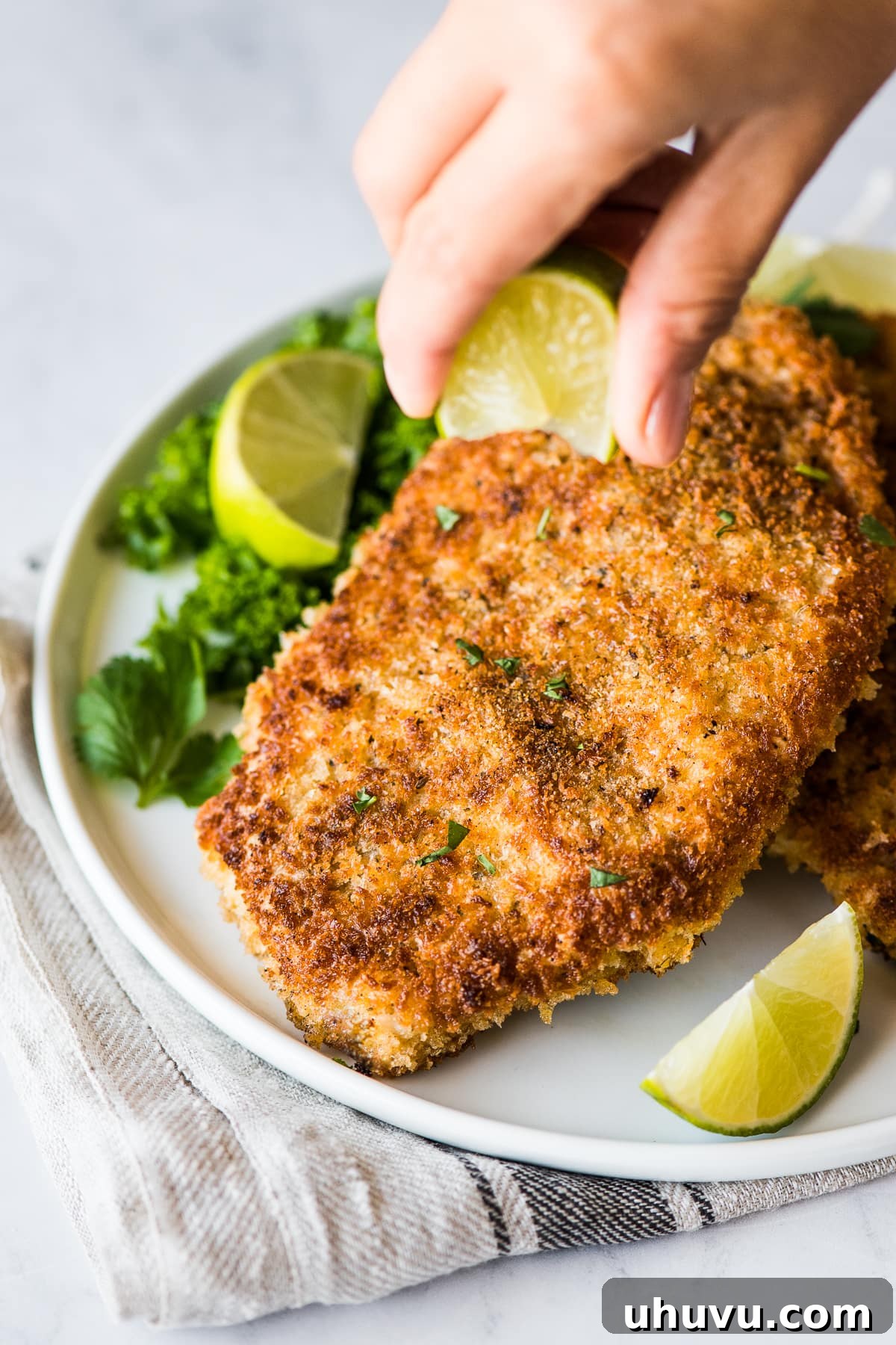 Plate of golden-brown crispy pork cutlets, with a fresh lime wedge being squeezed over them.