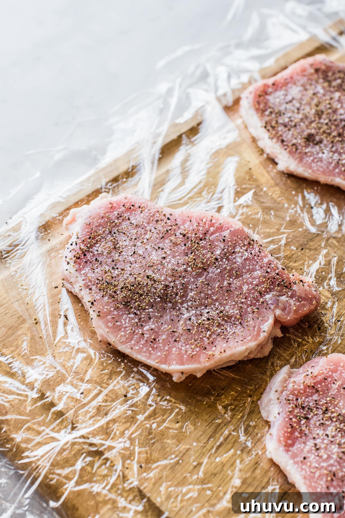 Pork chops, thinly pounded, seasoned with salt and pepper on a cutting board.