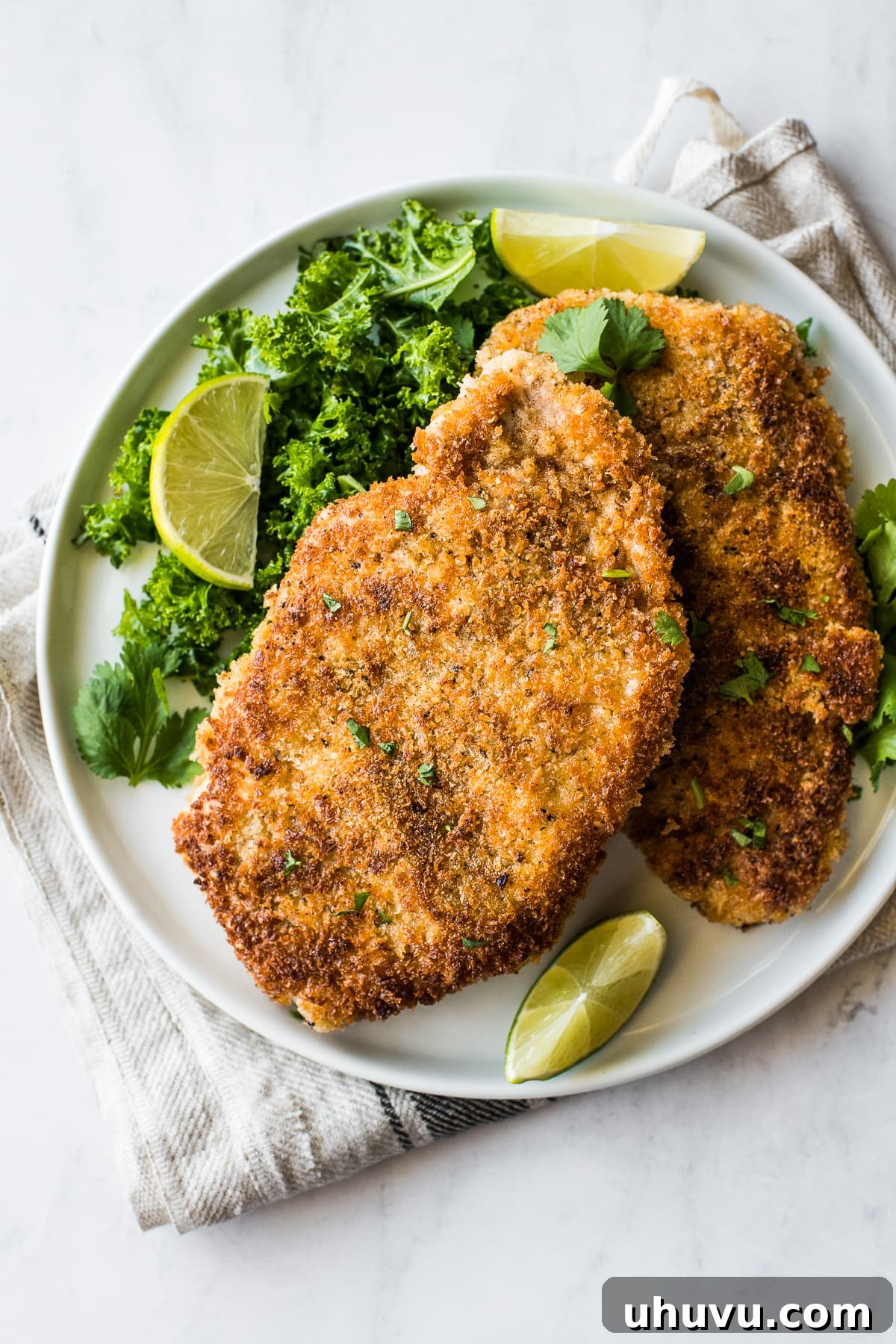 Serving of crispy pan-fried pork cutlets on a plate, garnished with fresh cilantro and lime wedges.