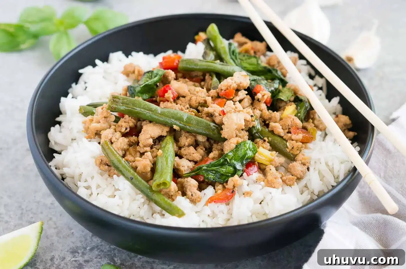 Close up image of Thai Basil Chicken stir-fry over rice in a bowl, showing vibrant colors and textures.