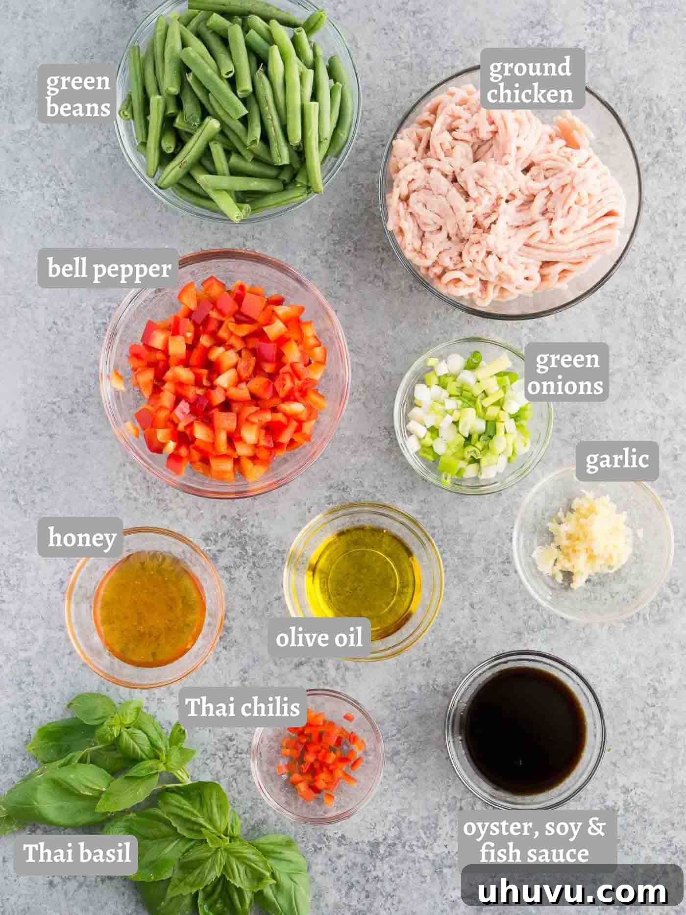 Assortment of fresh ingredients for Thai Basil Chicken stir fry, including chicken, sauces, chilies, and basil.