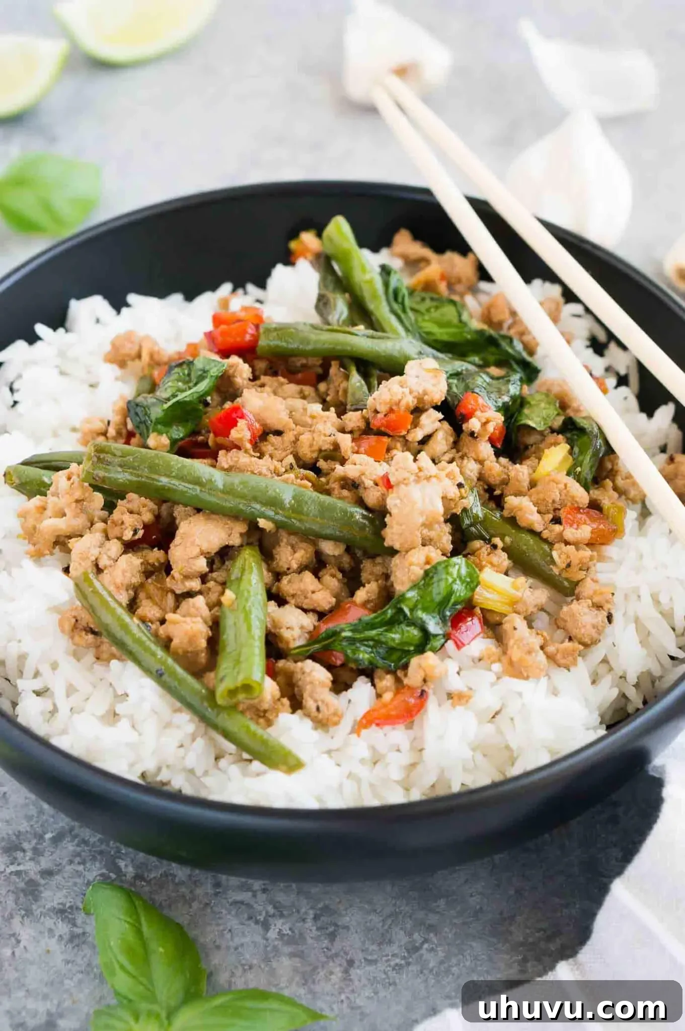 A generous serving of chicken with Thai basil over rice in a black bowl, ready to be eaten.