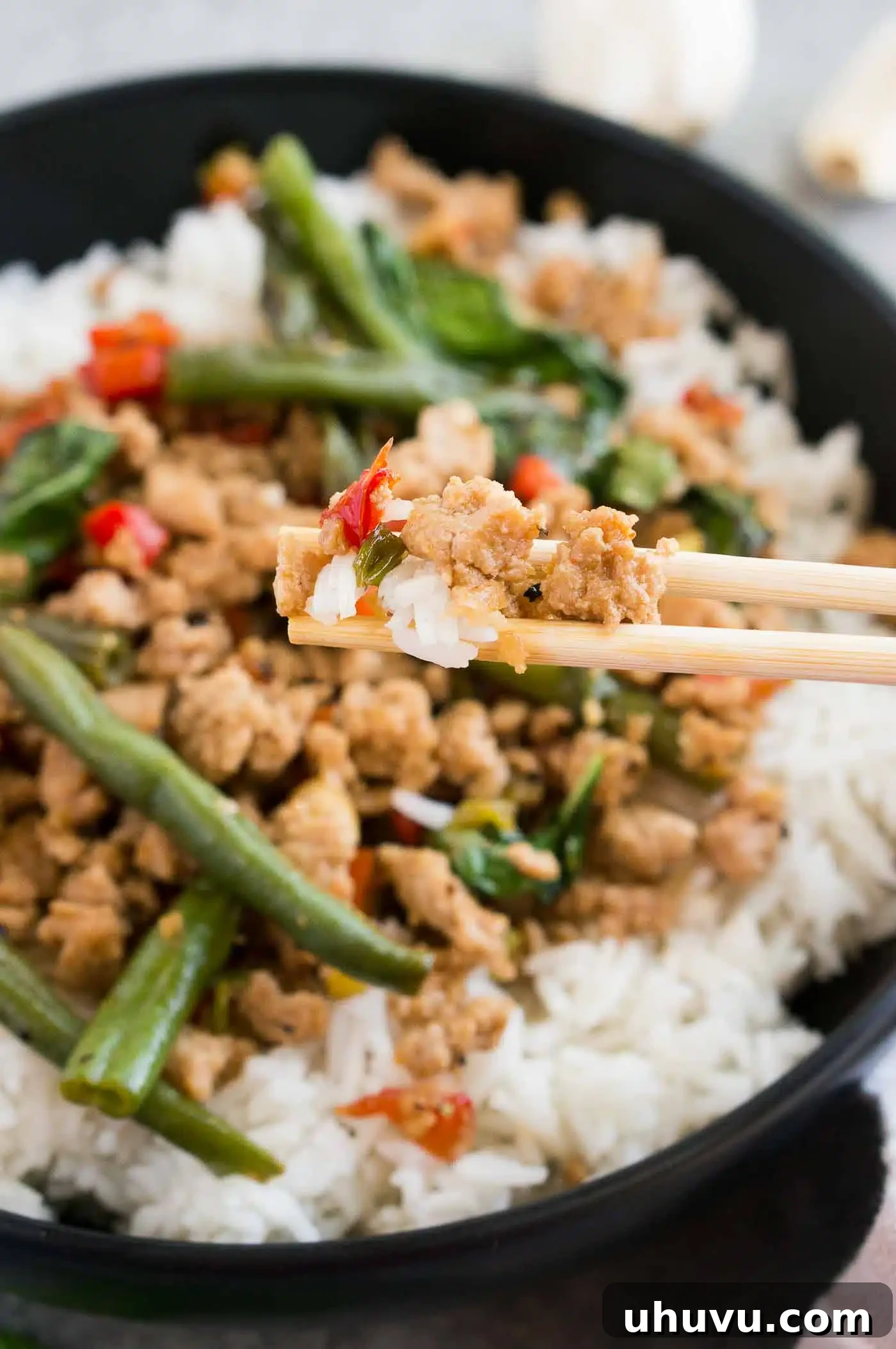 Person taking a bite of chicken stir fry with chopsticks, highlighting the deliciousness.