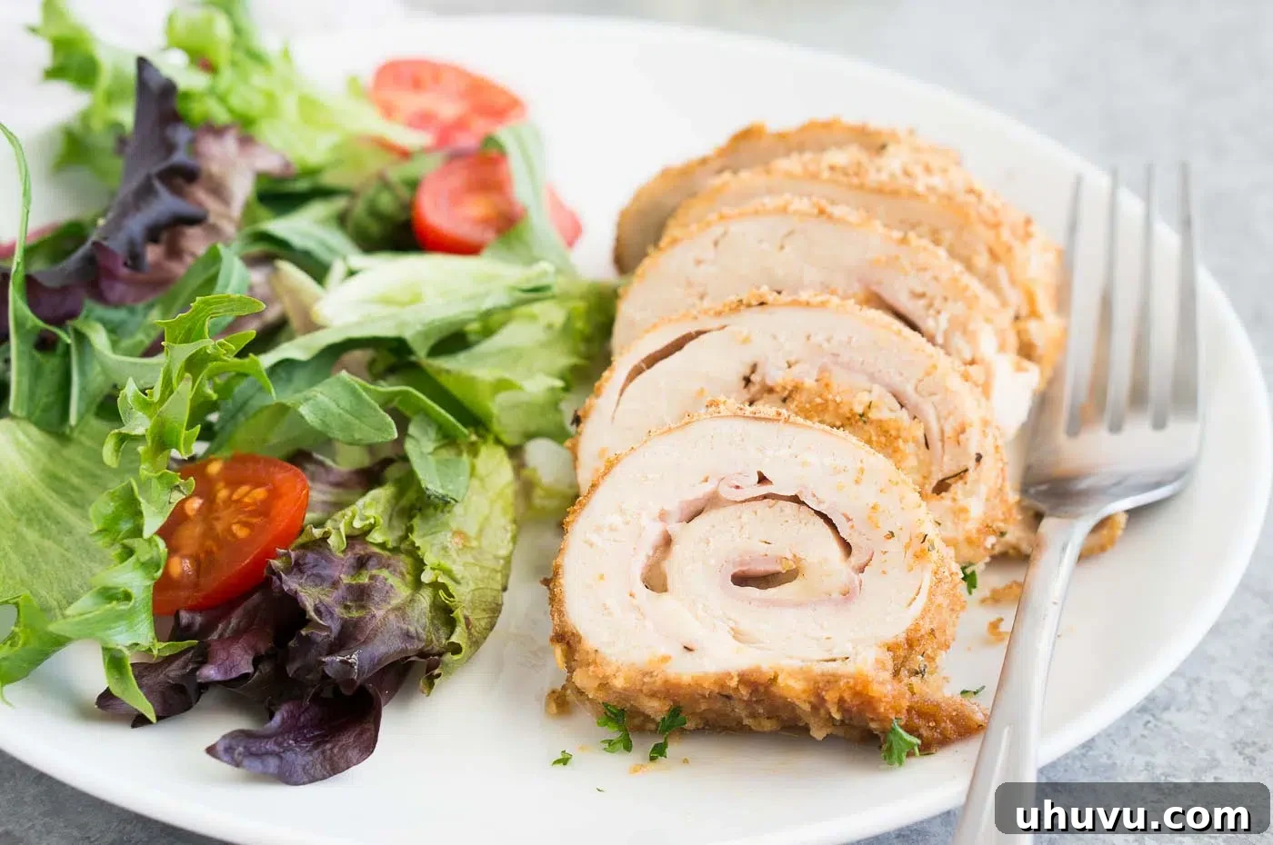Slices of oven-baked chicken cordon bleu revealing ham and melted cheese, served on a plate with fresh salad
