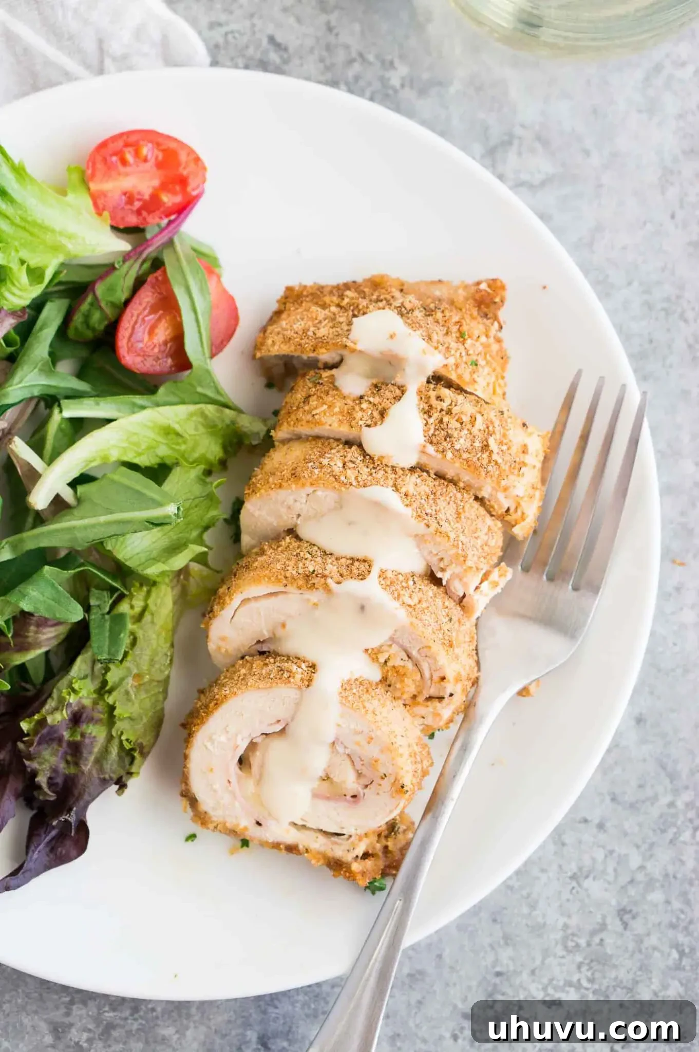 Close-up view of golden-brown chicken cordon bleu stuffed with ham and cheese, drizzled with creamy Dijon sauce on a dinner plate