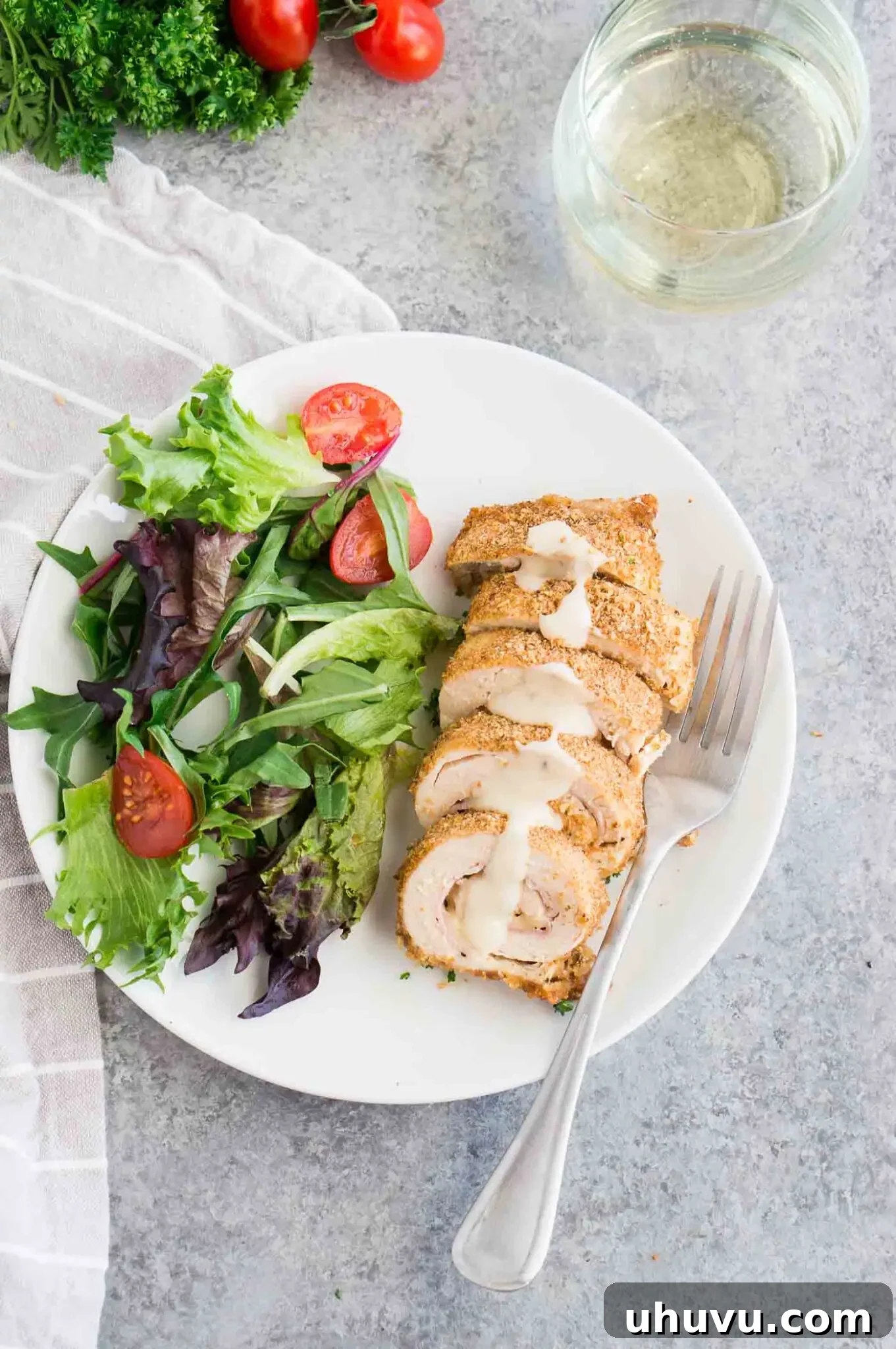A serving of golden-brown chicken cordon bleu with creamy Dijon sauce, accompanied by a fresh side salad on a white plate