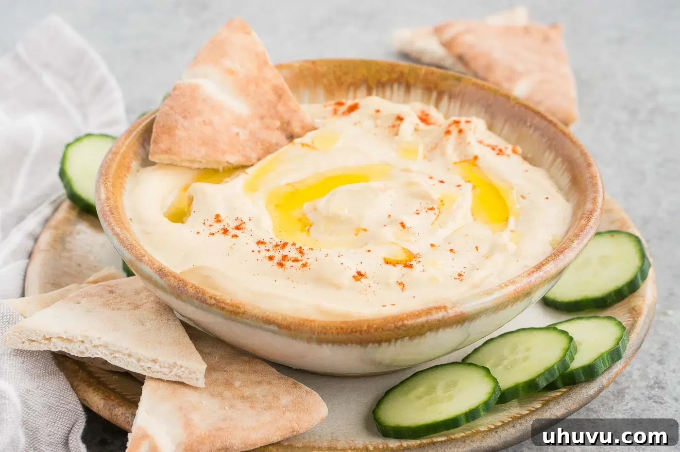 authentic hummus made at home served in a bowl with cucumber and pitas