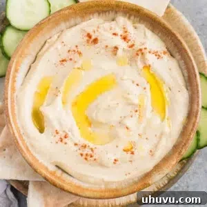 smooth and creamy hummus in a bowl with cucumbers and pita
