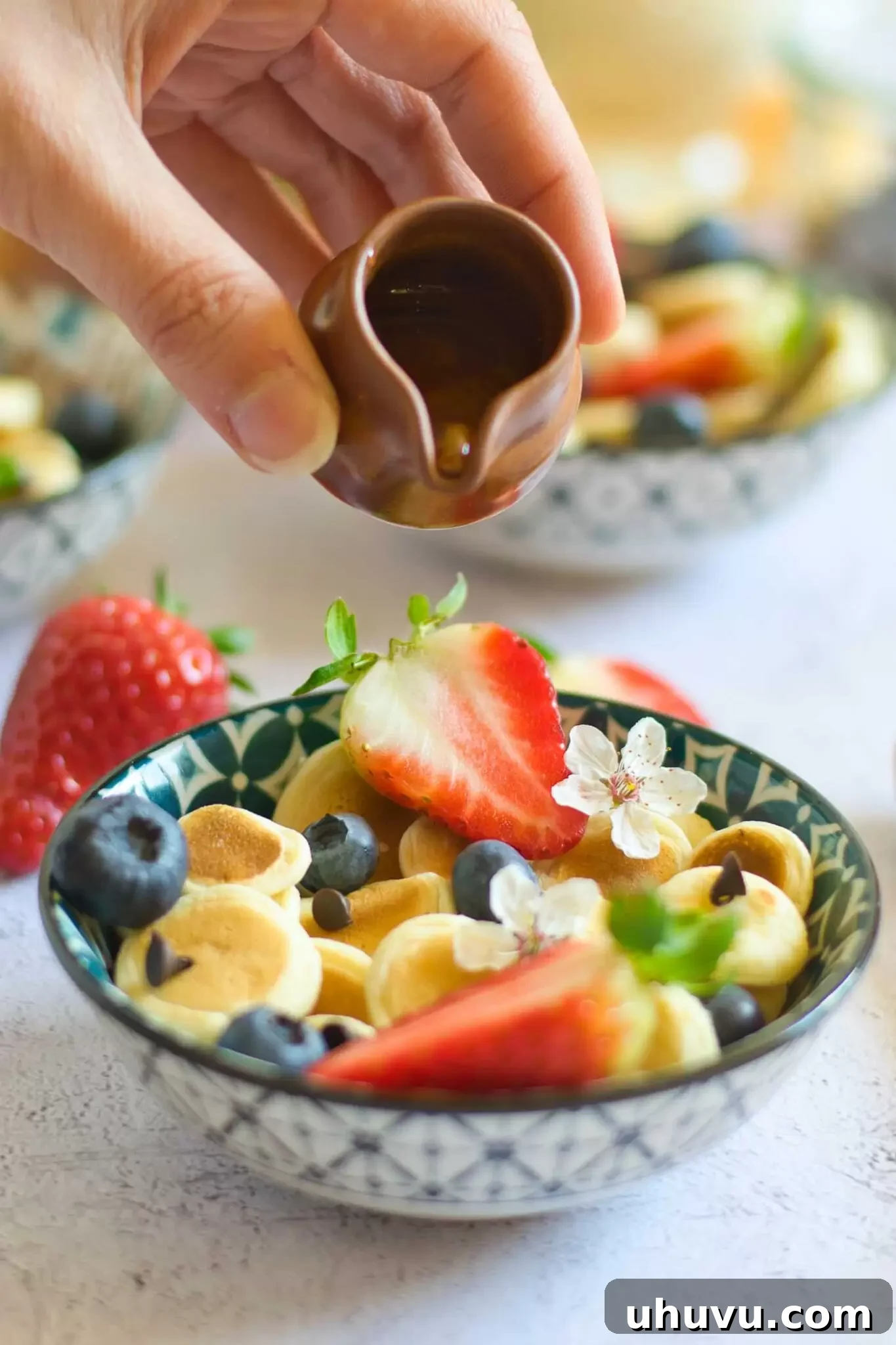 Hand pouring maple syrup over a bowl of pancake cereal.