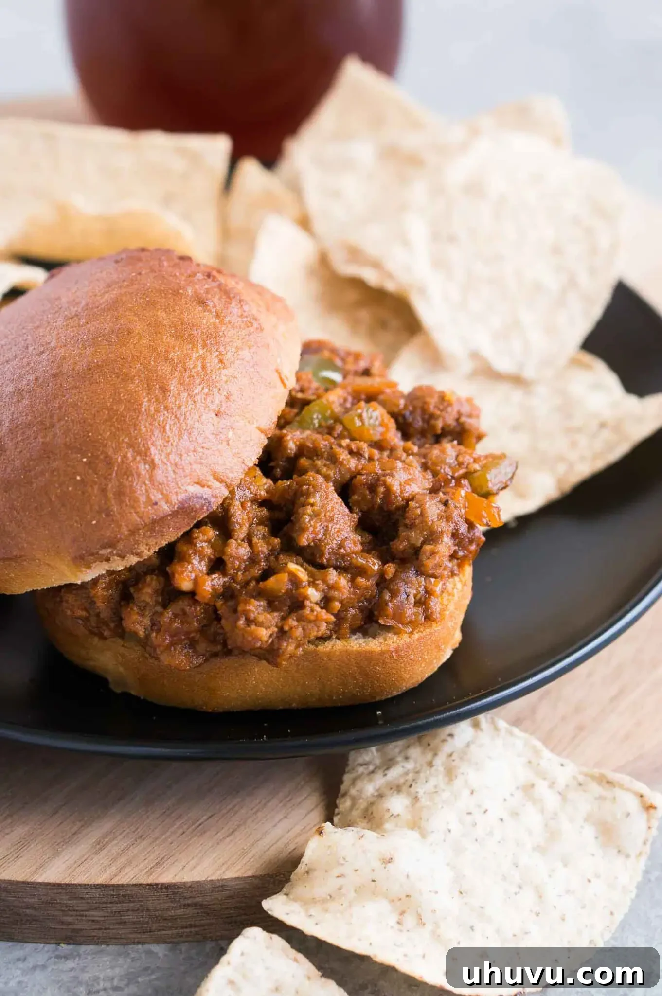 Easy homemade sloppy joe recipe served on a toasted bun with a side of crispy potato chips on a wooden board