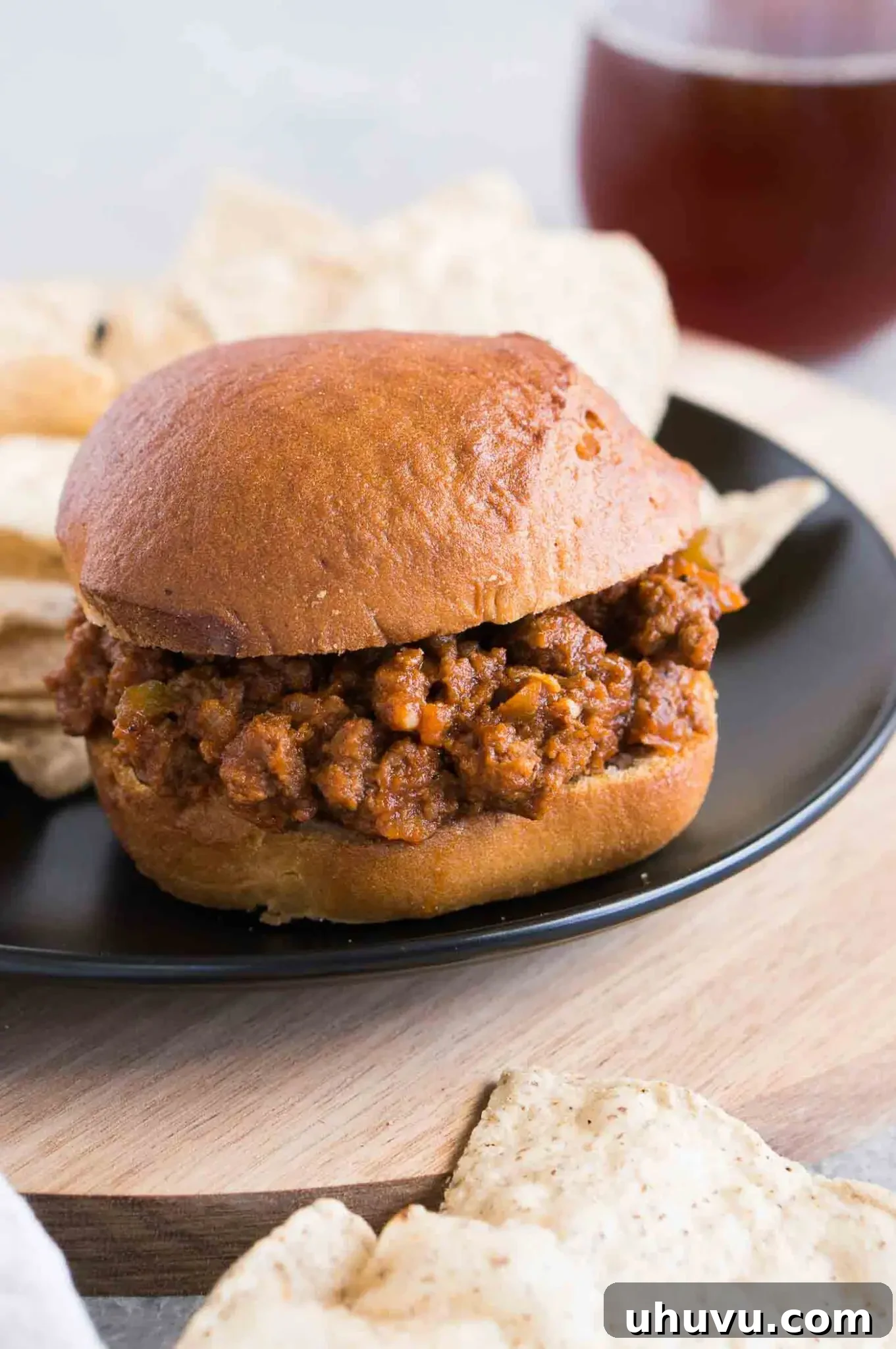 Sloppy Joes sandwich with melted cheese on a plate alongside crispy potato chips and a fork