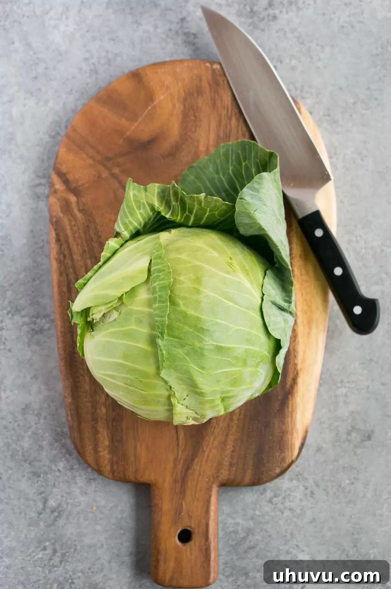 A fresh head of green cabbage resting on a wooden cutting board, ready for preparation