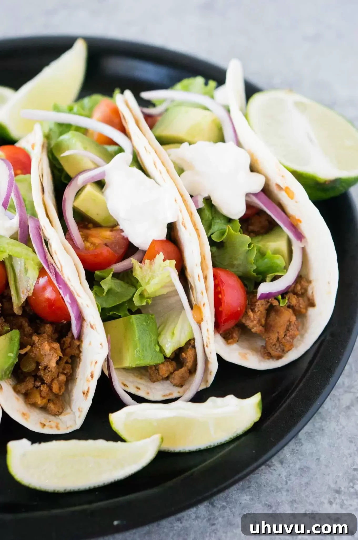 A close-up view of perfectly layered Mexican ground beef tacos, showcasing the vibrant toppings and rich filling.