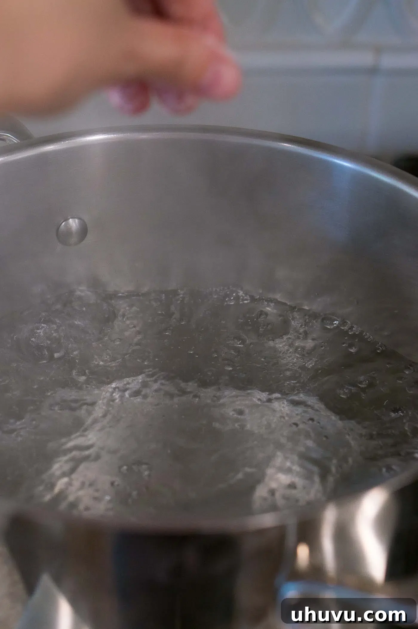 A large pot filled with water, vigorously boiling over a high heat burner on a stovetop.