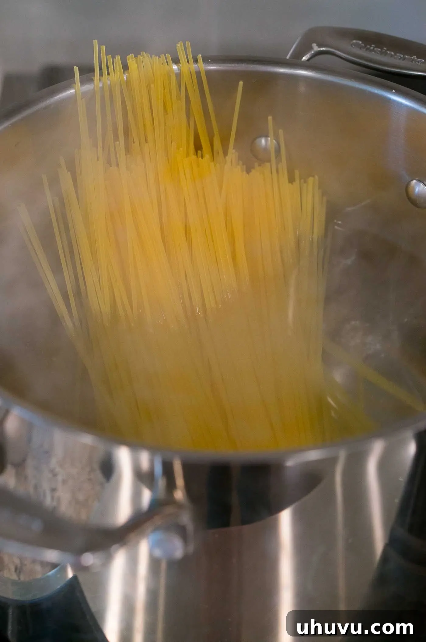 Dry spaghetti noodles being carefully added into a large pot of vigorously boiling, salted water.