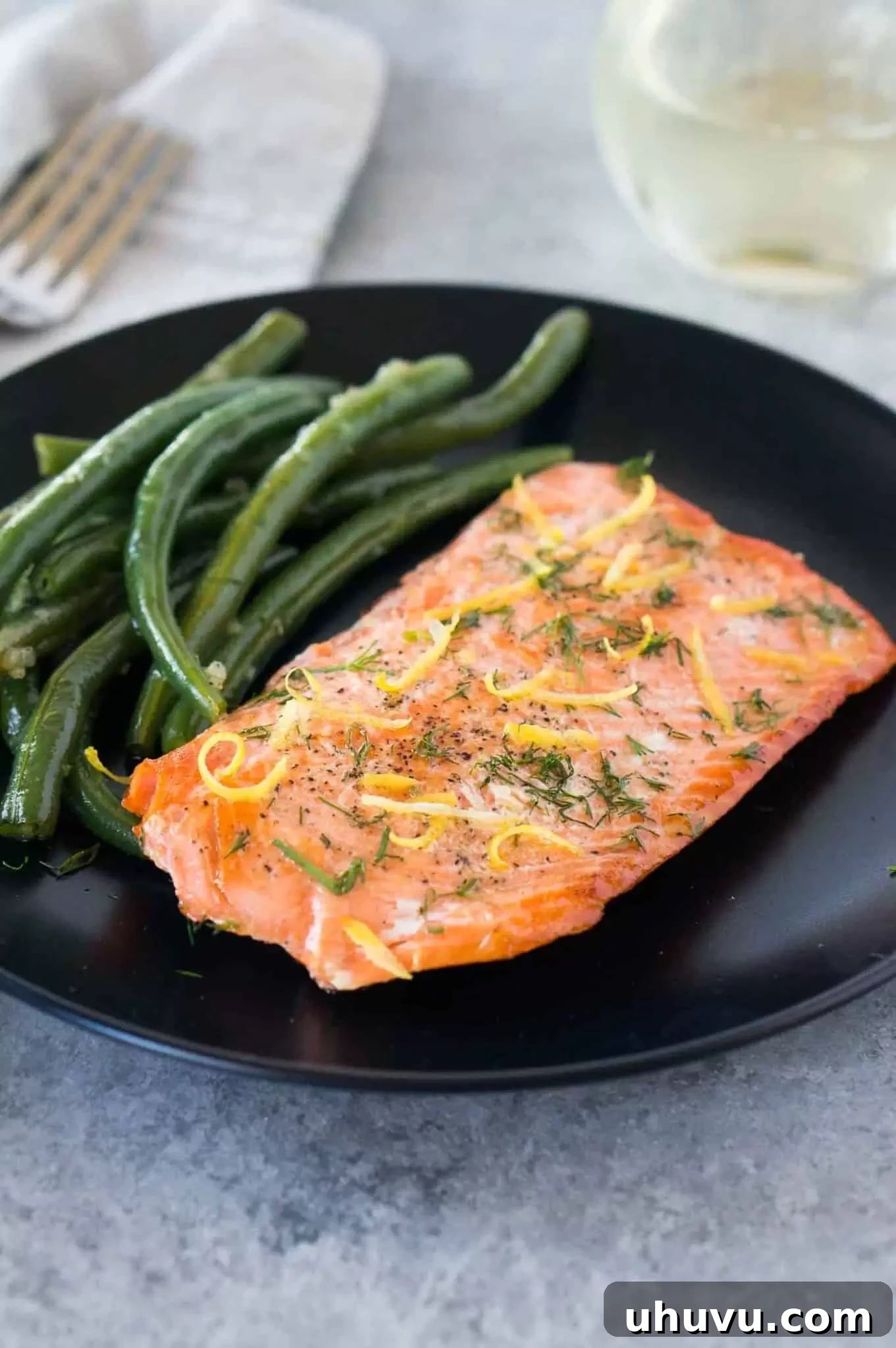 The Ultimate Sous Vide Salmon 2 Serve sous vide salmon on a plate with vibrant green beans, garnished with fresh herbs and lemon slices.