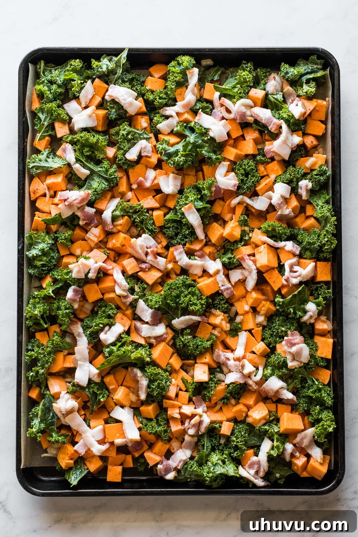 Sheet Pan Breakfast Bake 4 Sweet potatoes, kale, and bacon spread evenly on a sheet pan before baking.