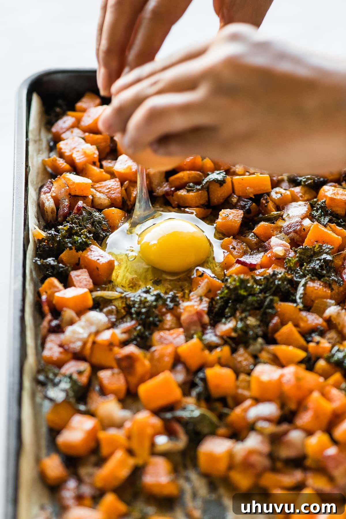 Sheet Pan Breakfast Bake 5 A fresh egg being cracked directly into a designated well on a sheet pan filled with breakfast hash.