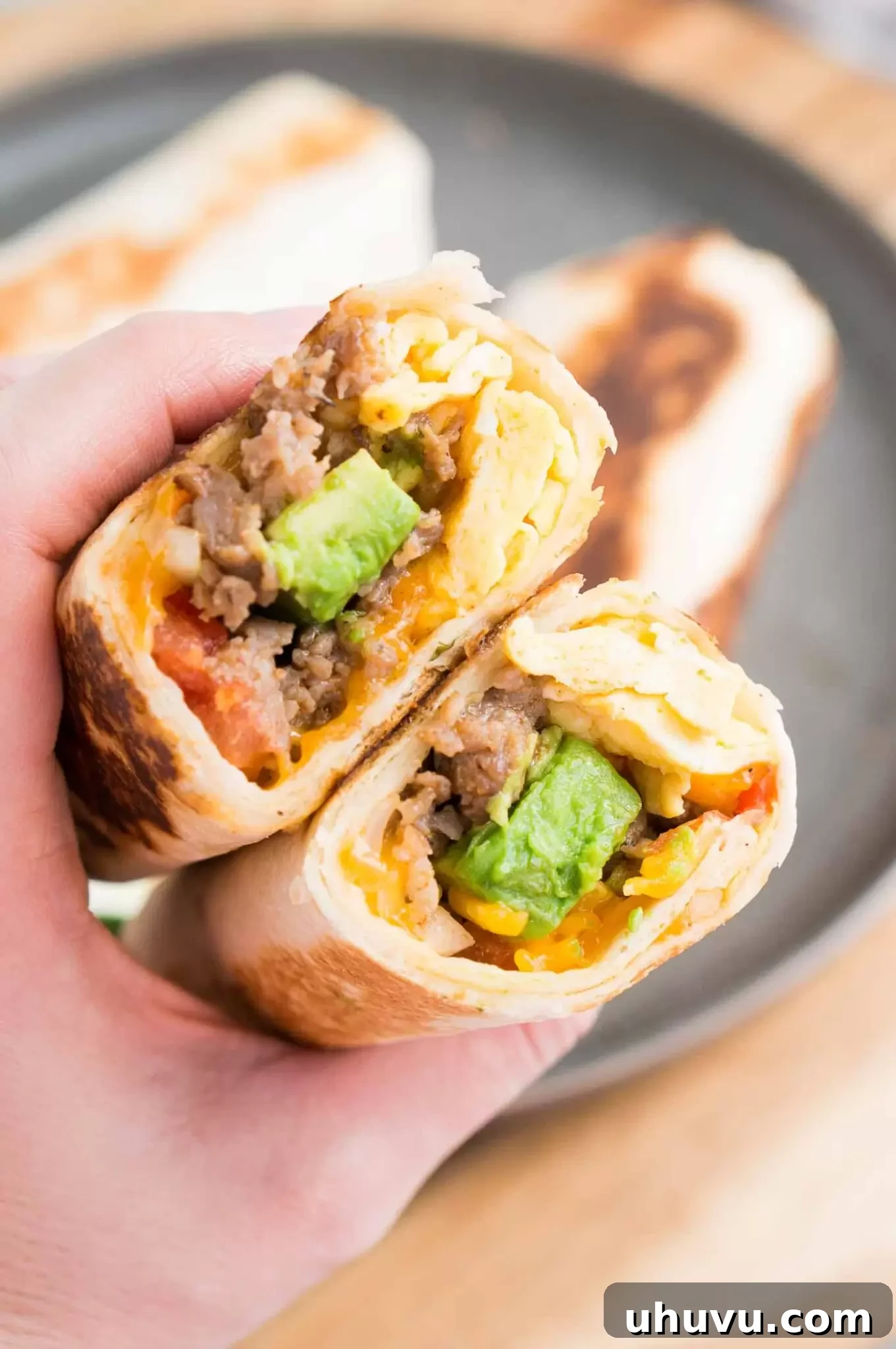 Two perfectly rolled breakfast burritos stacked on a cutting board