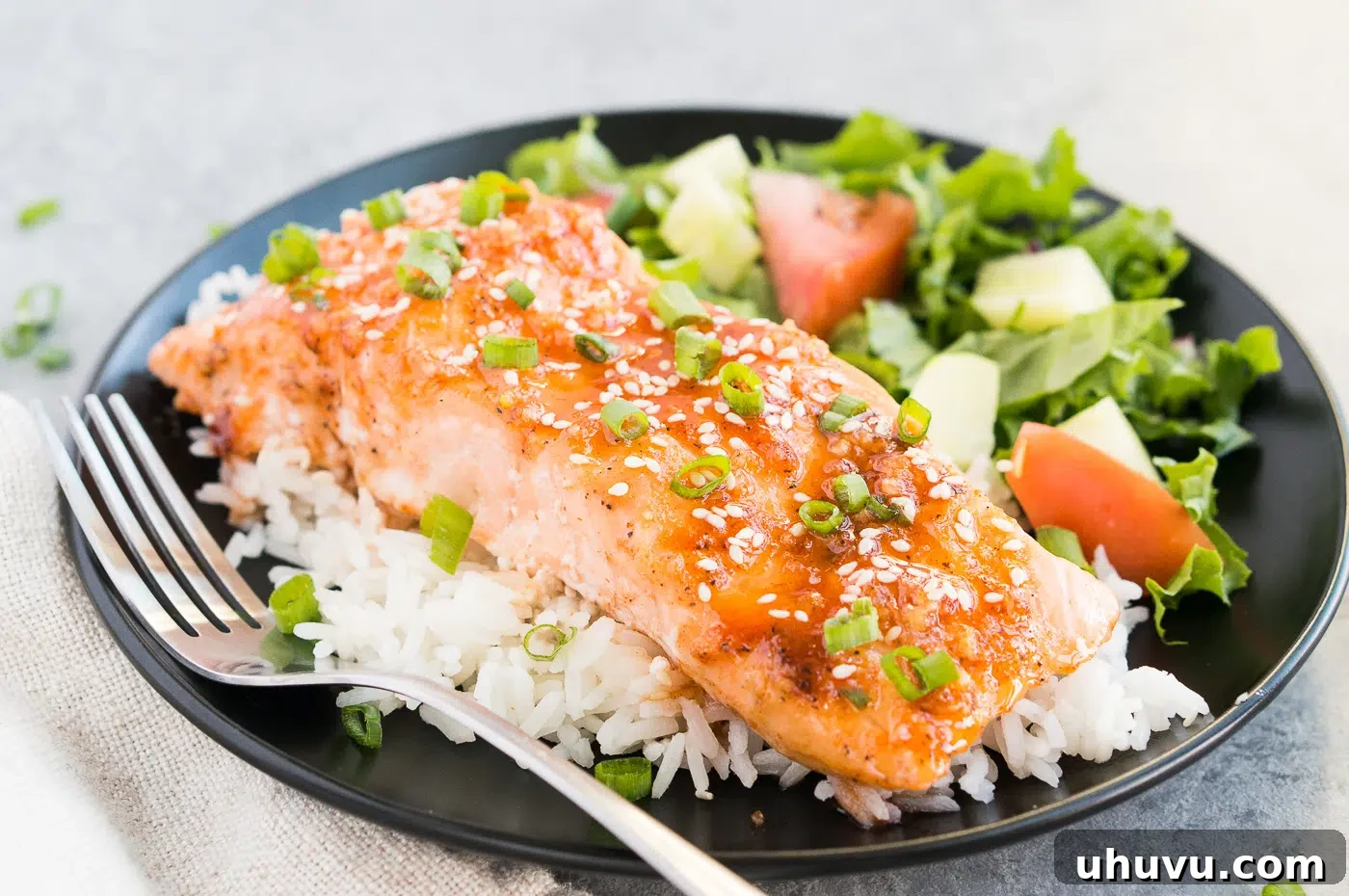 Plated honey glazed salmon served over rice with a fresh green salad on a black plate, showcasing a complete and healthy meal.