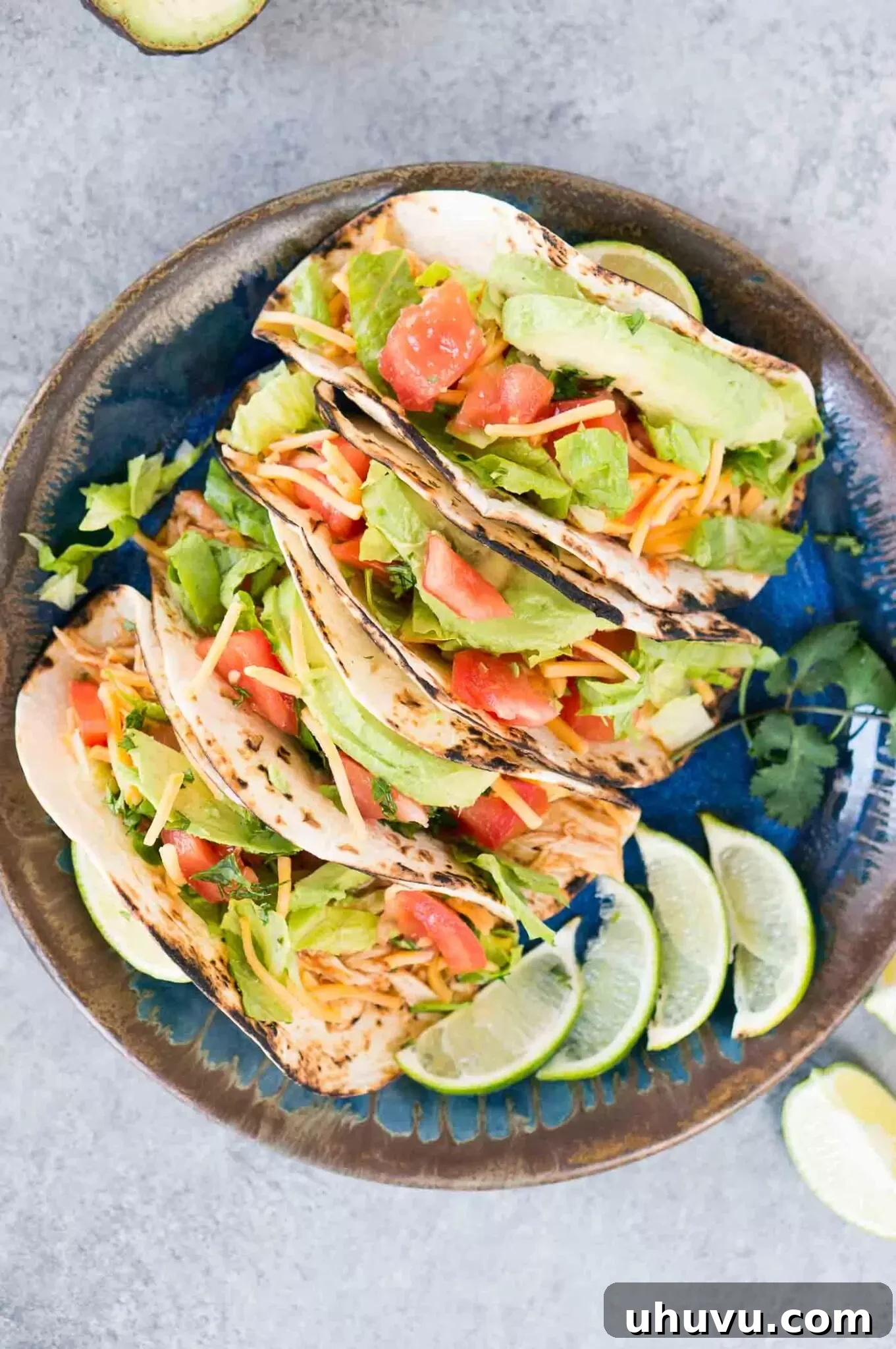 chicken tacos with lettuce, tomatoes, avocado and cheese on a plate