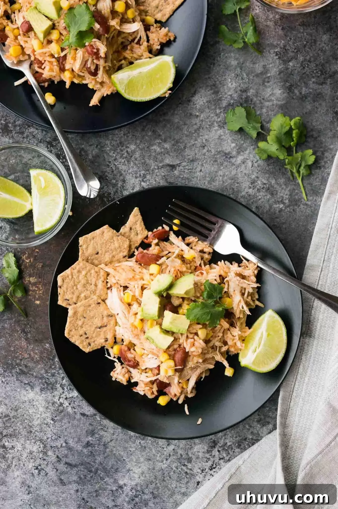 A bowl of chicken, rice, beans, and corn garnished on a black plate, showcasing its vibrant ingredients.