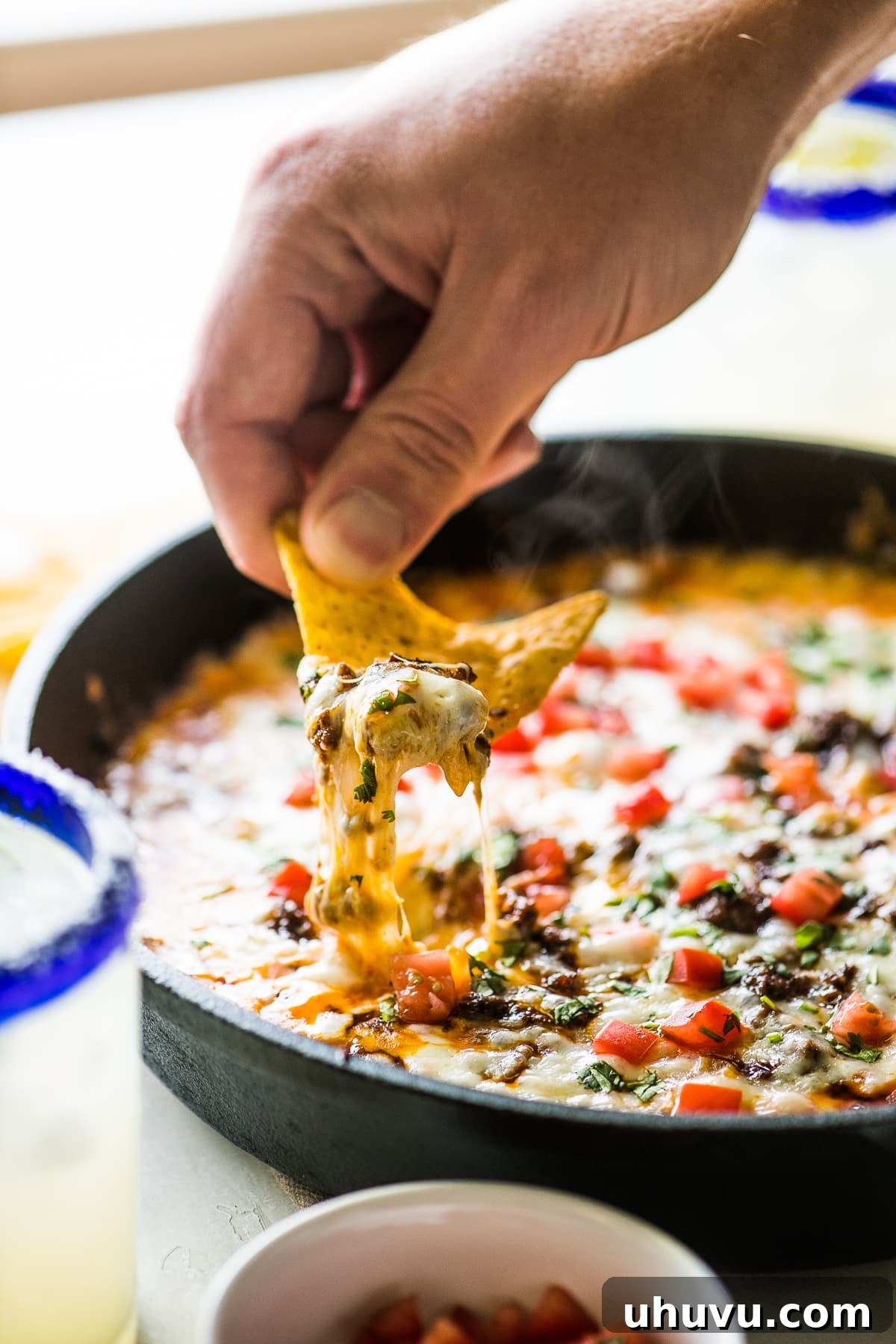 Ultimate Cheese Dip 5 A tortilla chip being dipped in queso fundido, showcasing its gooey texture.