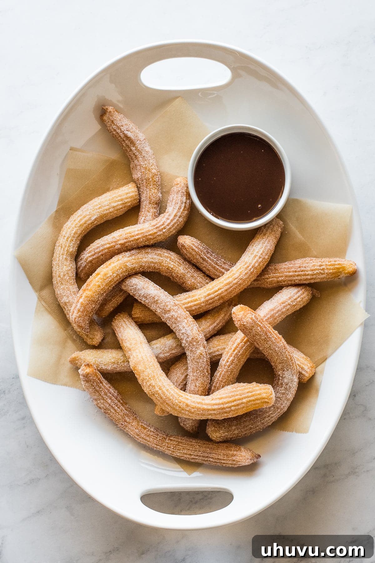 Authentic Churros From Scratch 4 Churros covered in cinnamon sugar with a ramekin of chocolate sauce.