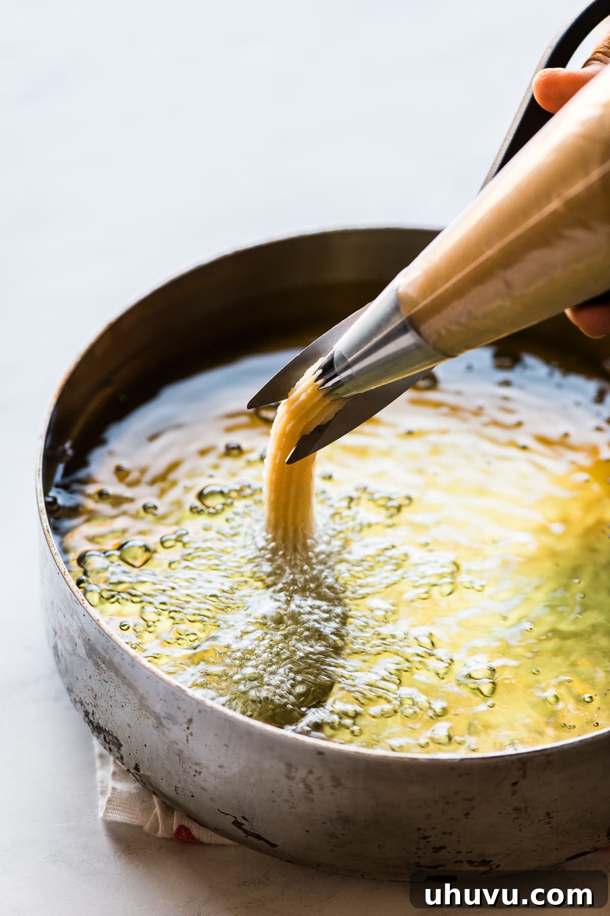 Authentic Churros From Scratch 6 Churros being piped in hot oil for frying.