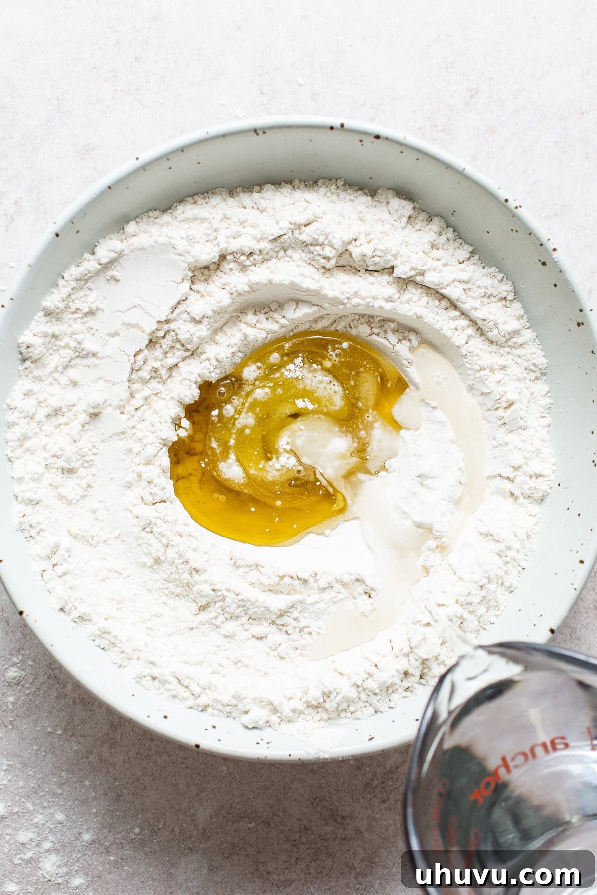 Flour, olive oil, warm water, and baking powder are combined in a large mixing bowl to make tortilla dough.