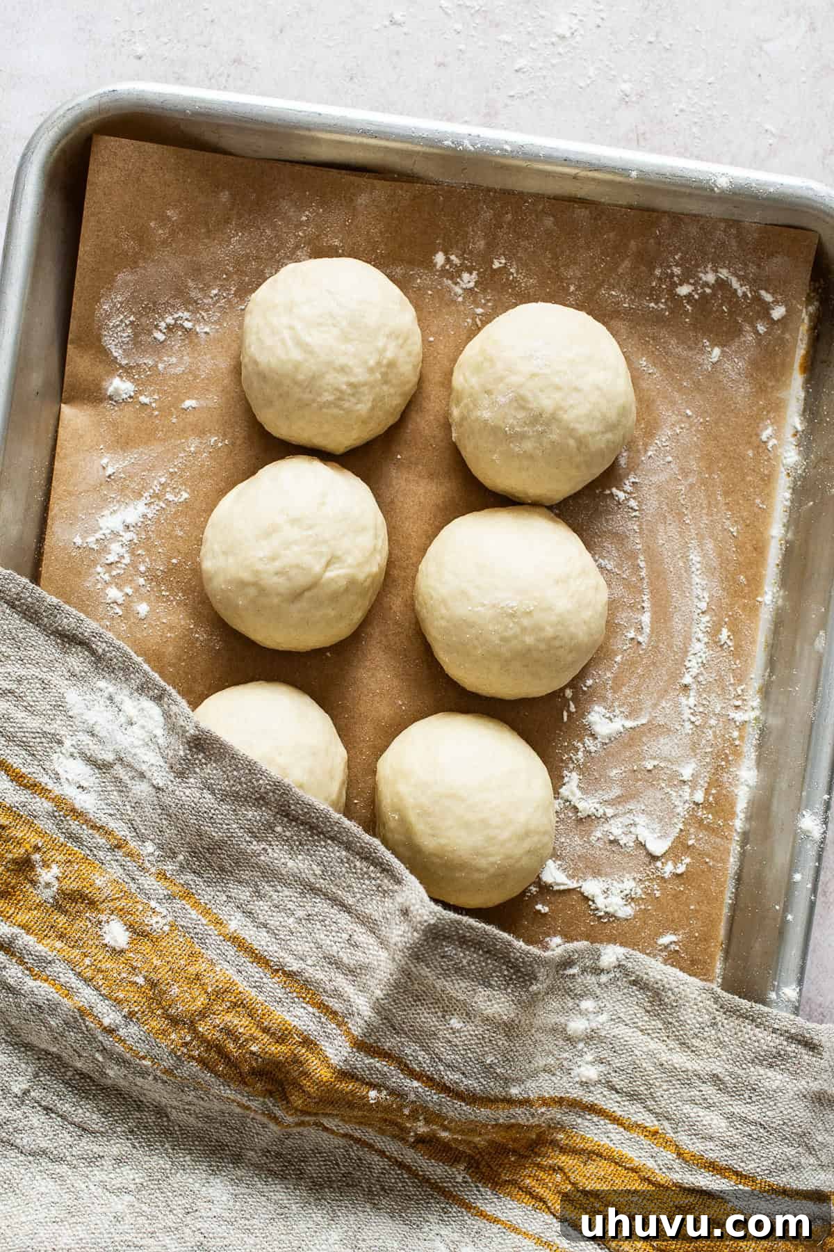 Eight equal balls of flour tortilla dough, covered with a kitchen towel and resting on a baking sheet