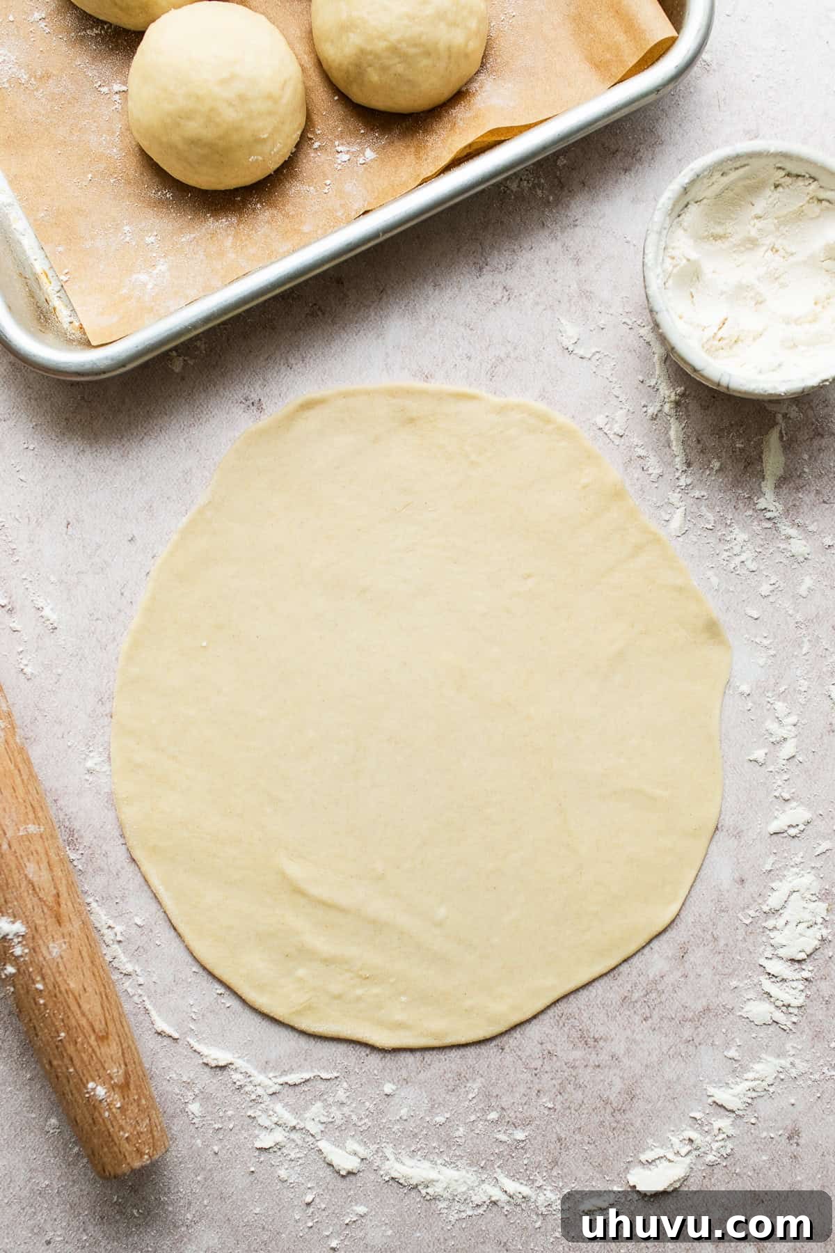 A single ball of flour tortilla dough being expertly rolled out into a perfect circle on a floured surface