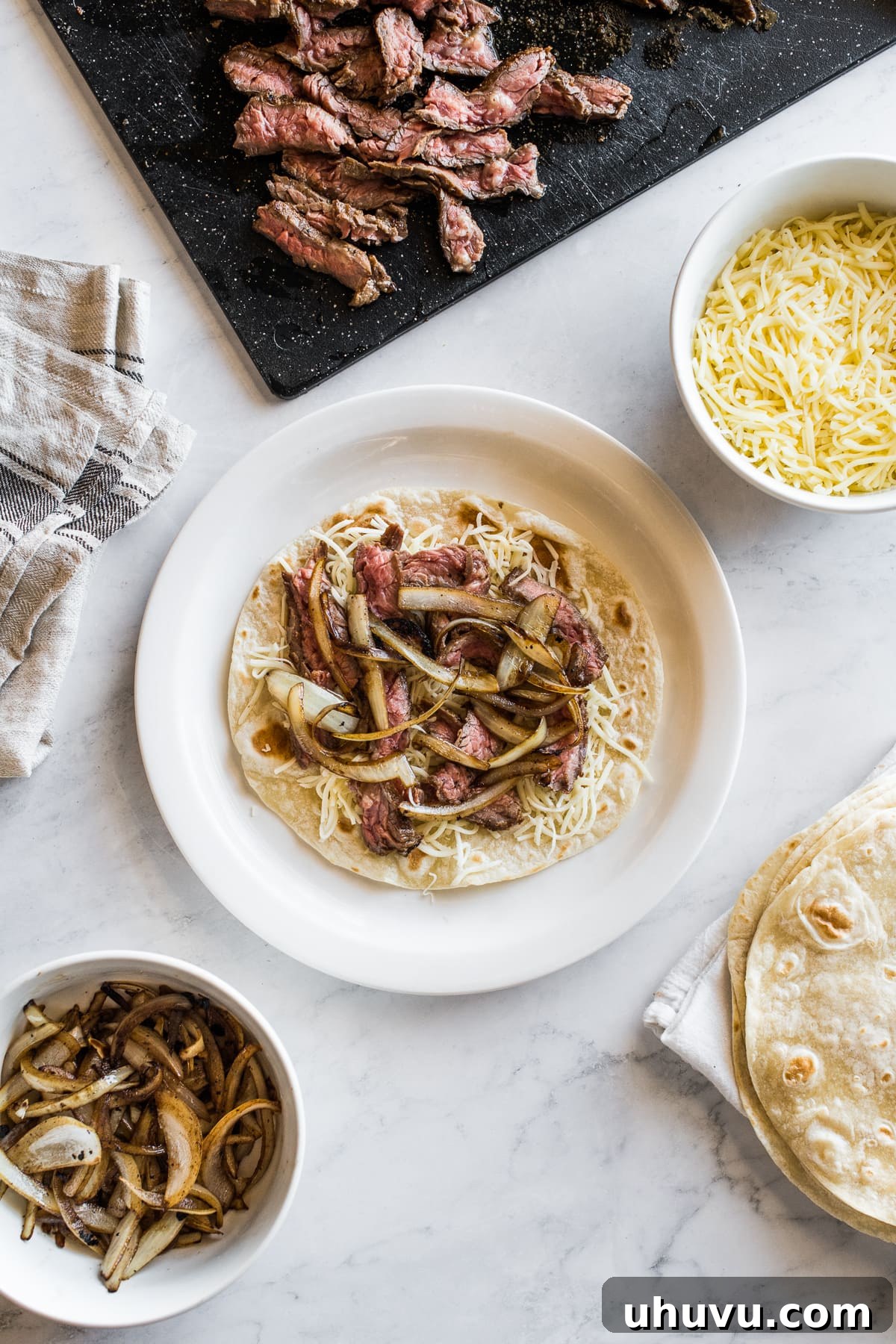 Gourmet Steak Quesadillas 4 A steak quesadilla being assembled with sliced steak, shredded cheese, and sauteed onions on a tortilla.