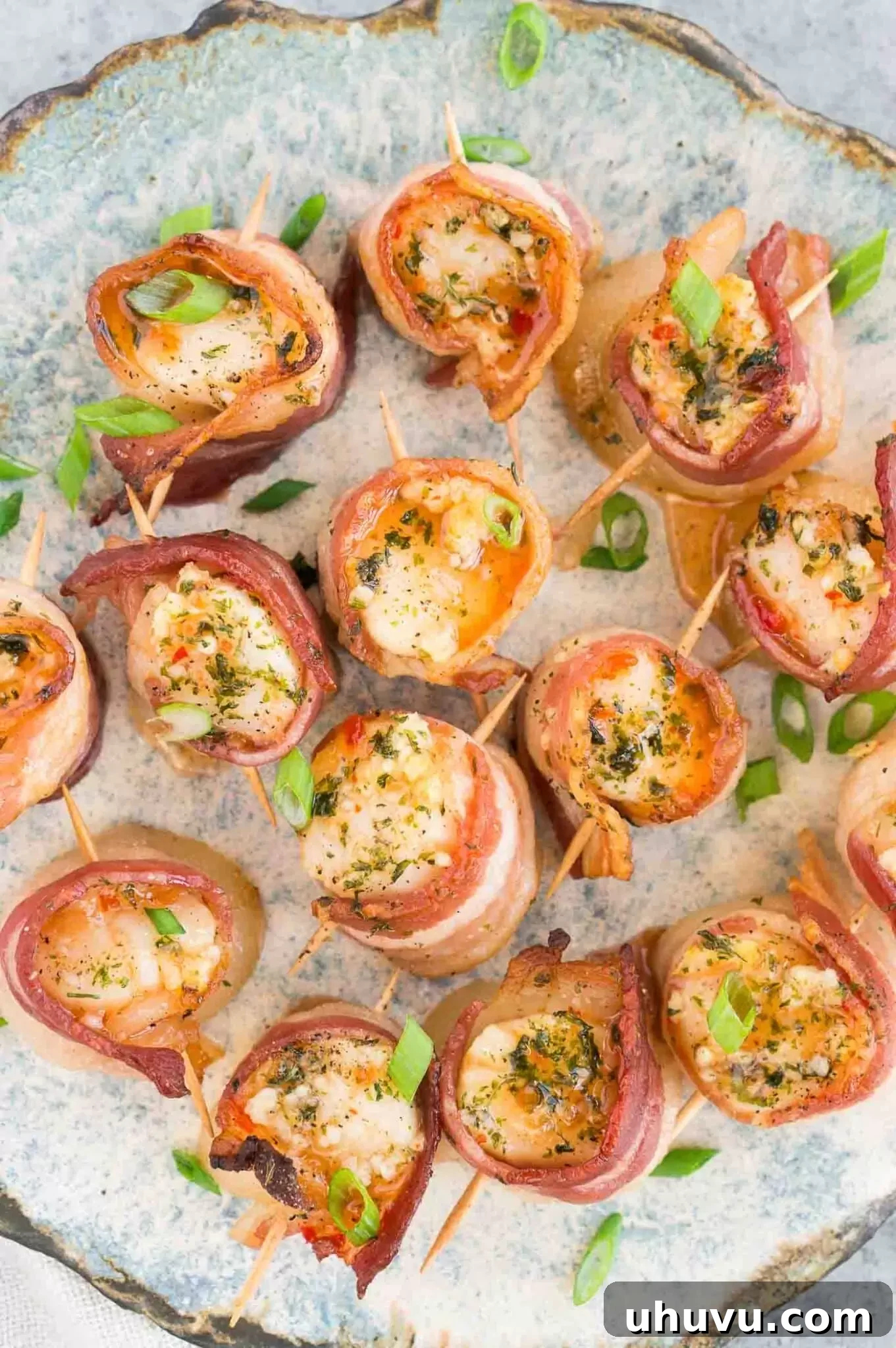 A vibrant plate of bacon wrapped scallops, glazed with pepper jelly and garnished, presented as an elegant appetizer.