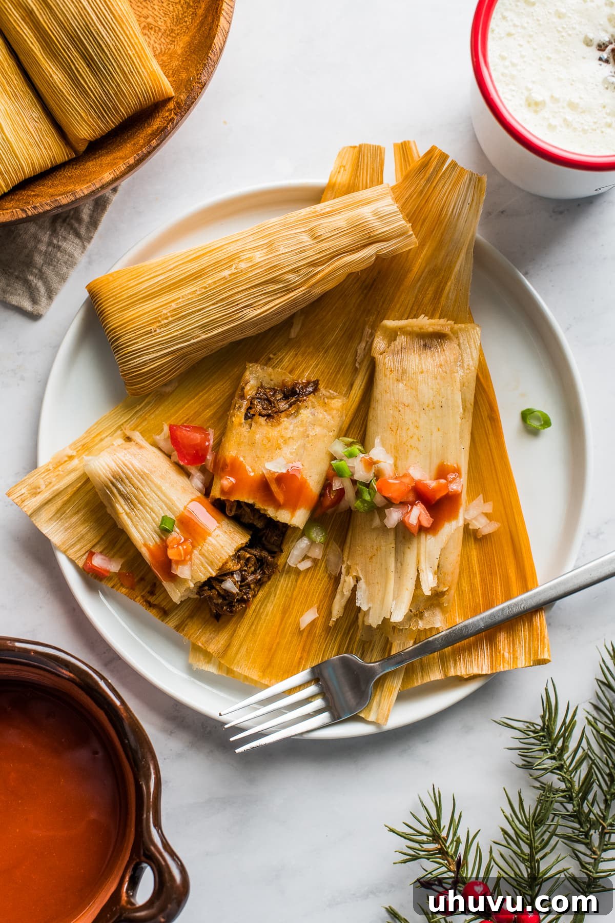 Instant Pot Tamales on a plate topped with fresh tomatoes and onions.