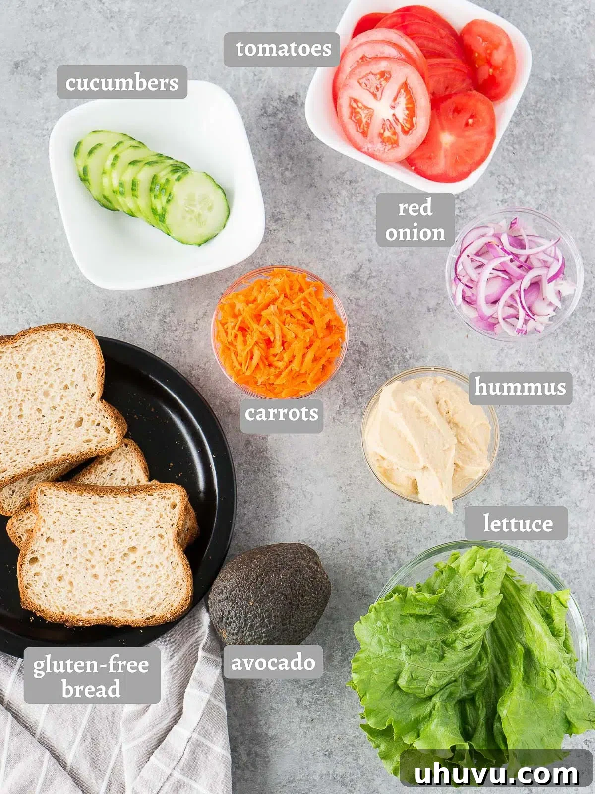 A vibrant selection of fresh ingredients including bread, hummus, lettuce, tomato, cucumber, carrots, red onion, and avocado, perfectly arranged for a healthy veggie sandwich.