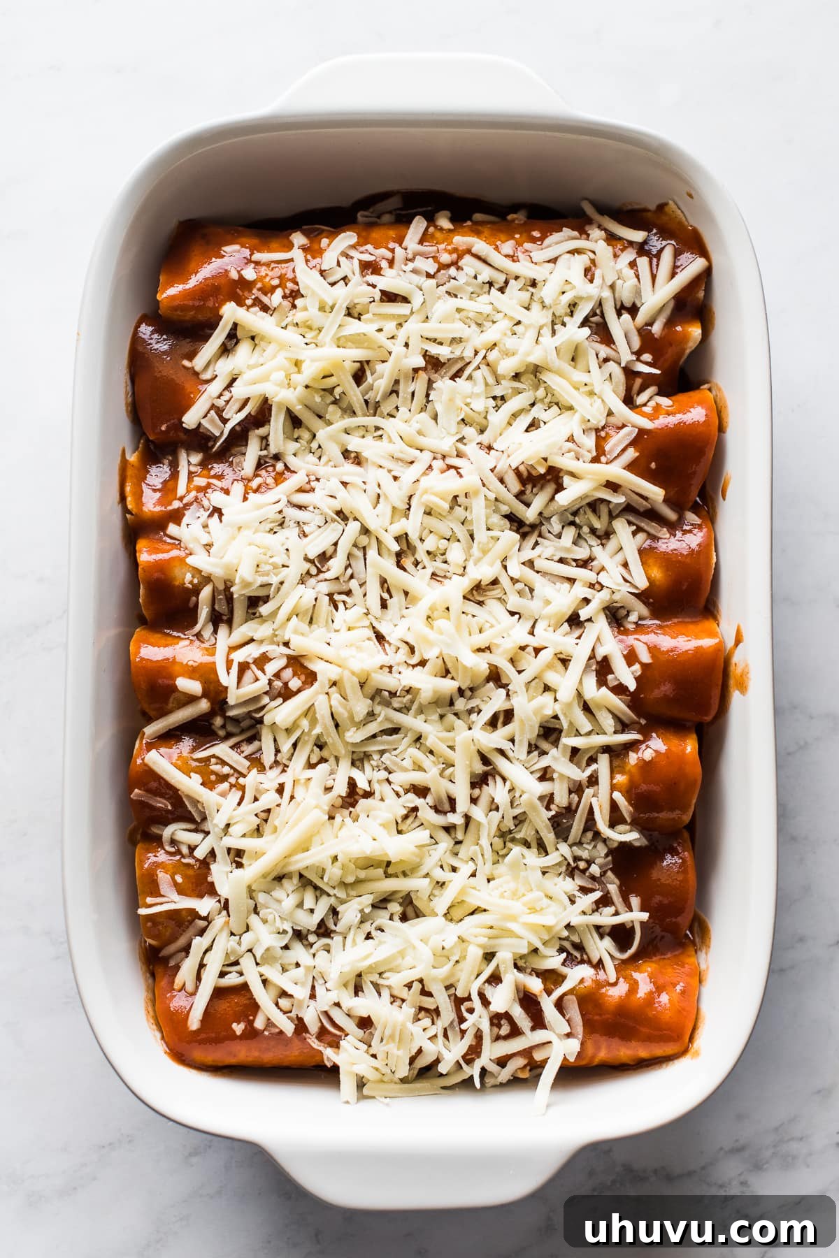 Savory Turkey Enchilada Bake 3 Unbaked Turkey Enchiladas arranged in a casserole dish, lavishly topped with an extra layer of shredded cheese, ready for the oven.
