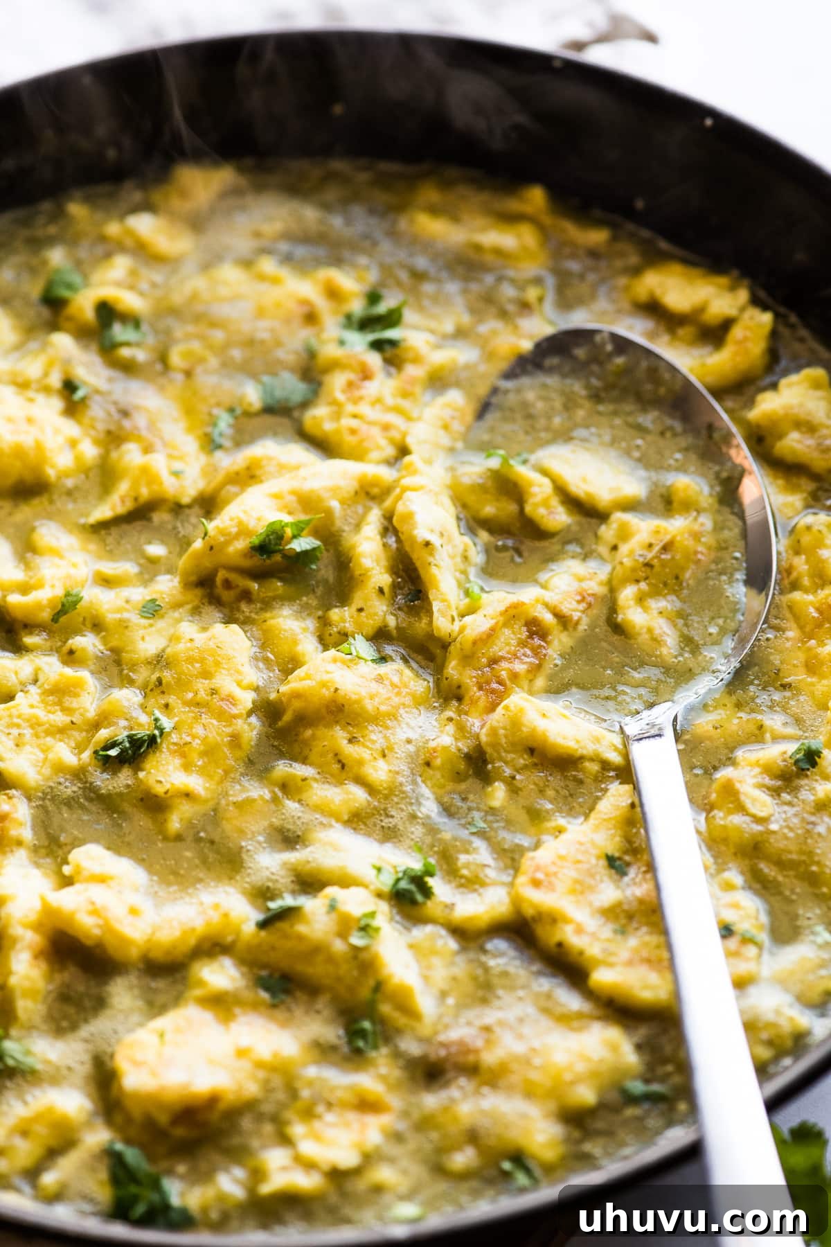 Green Chile Egg Delight 5 Scrambled eggs luxuriating in a vibrant salsa verde, gently simmering in a skillet, showcasing the rich colors and textures of the dish.