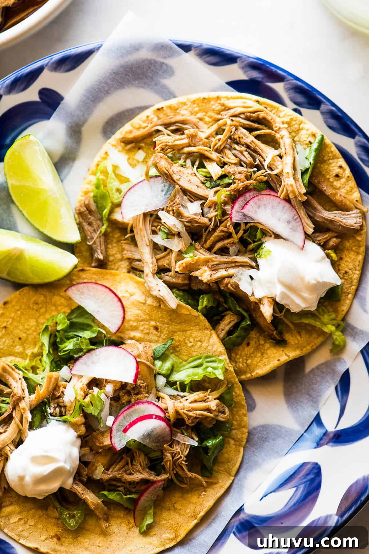 Speedy Instant Pot Chicken Tacos 5 Two instant pot chicken tacos served on a plate with limes and radishes as toppings.