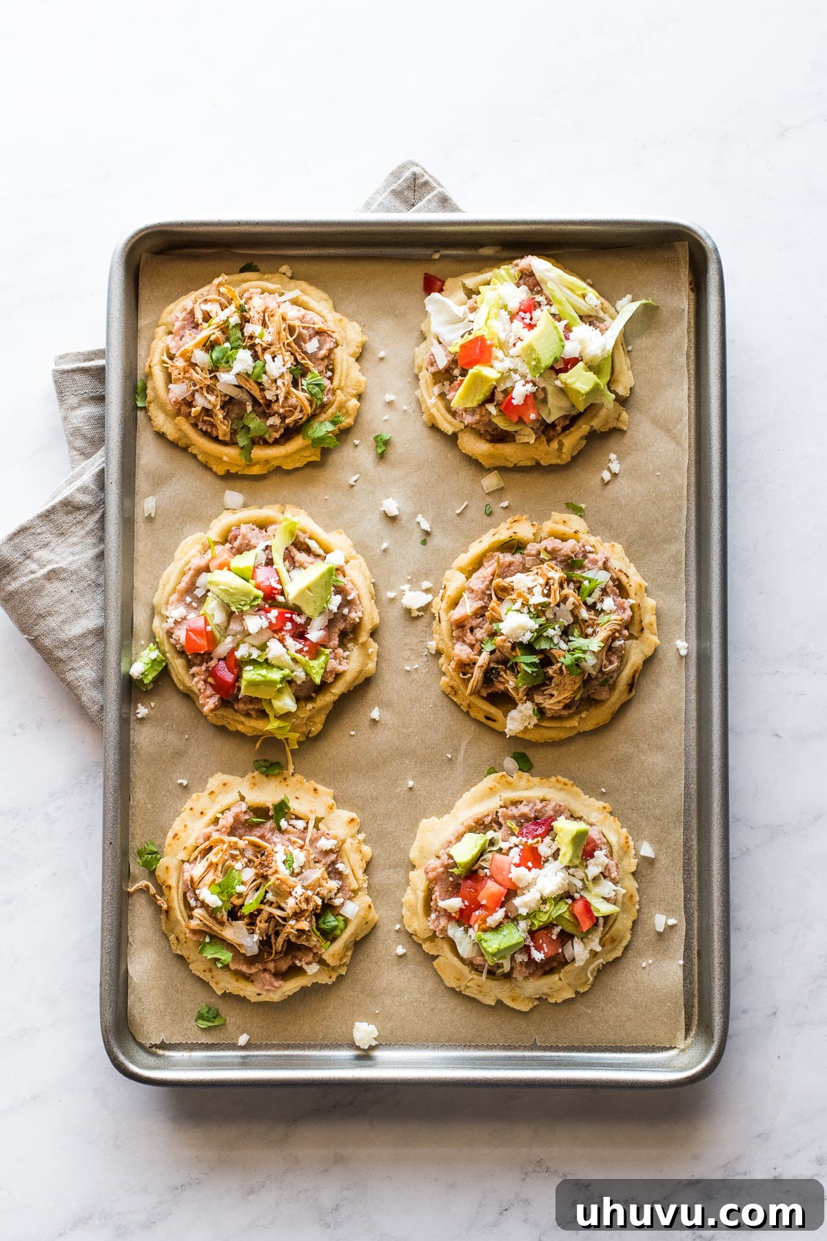 Sopes 3 Mexican sopes topped with various toppings on a baking sheet.
