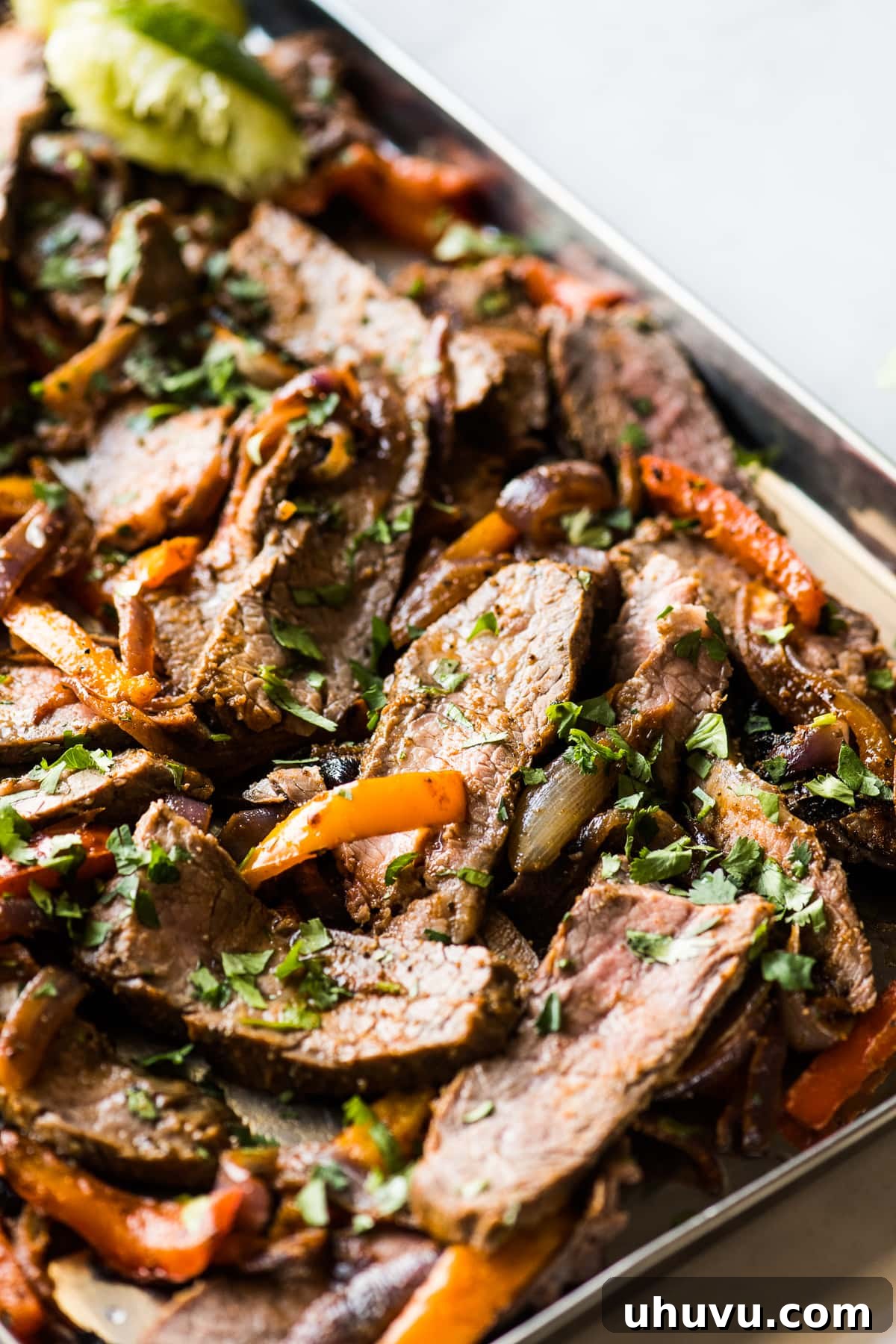 A sheet pan filled with perfectly sliced steak fajitas, vibrant bell peppers, and onions, ready for assembly.