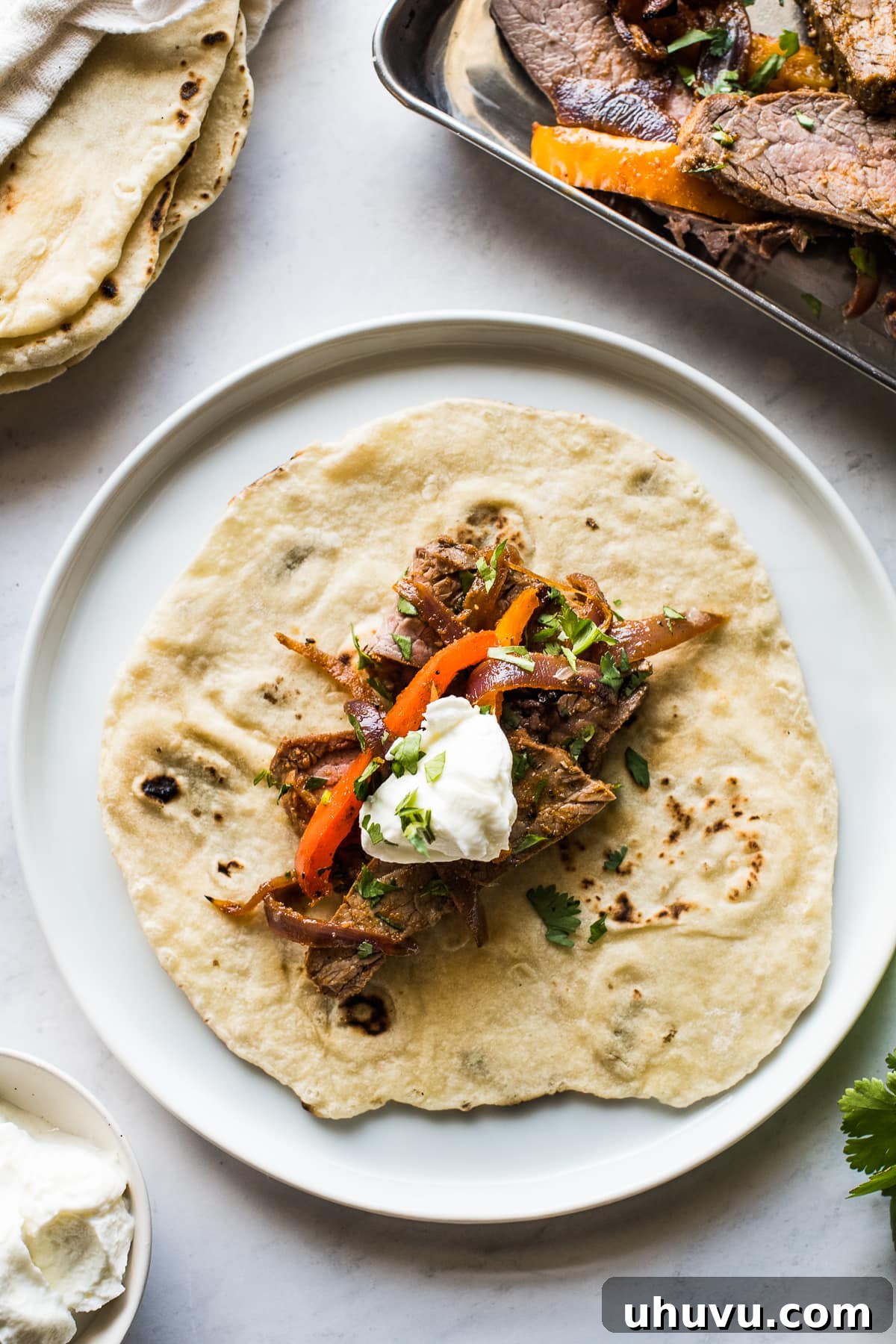 A delicious sheet pan steak fajita on a warm flour tortilla, generously topped with a dollop of sour cream and a sprinkle of fresh cilantro.