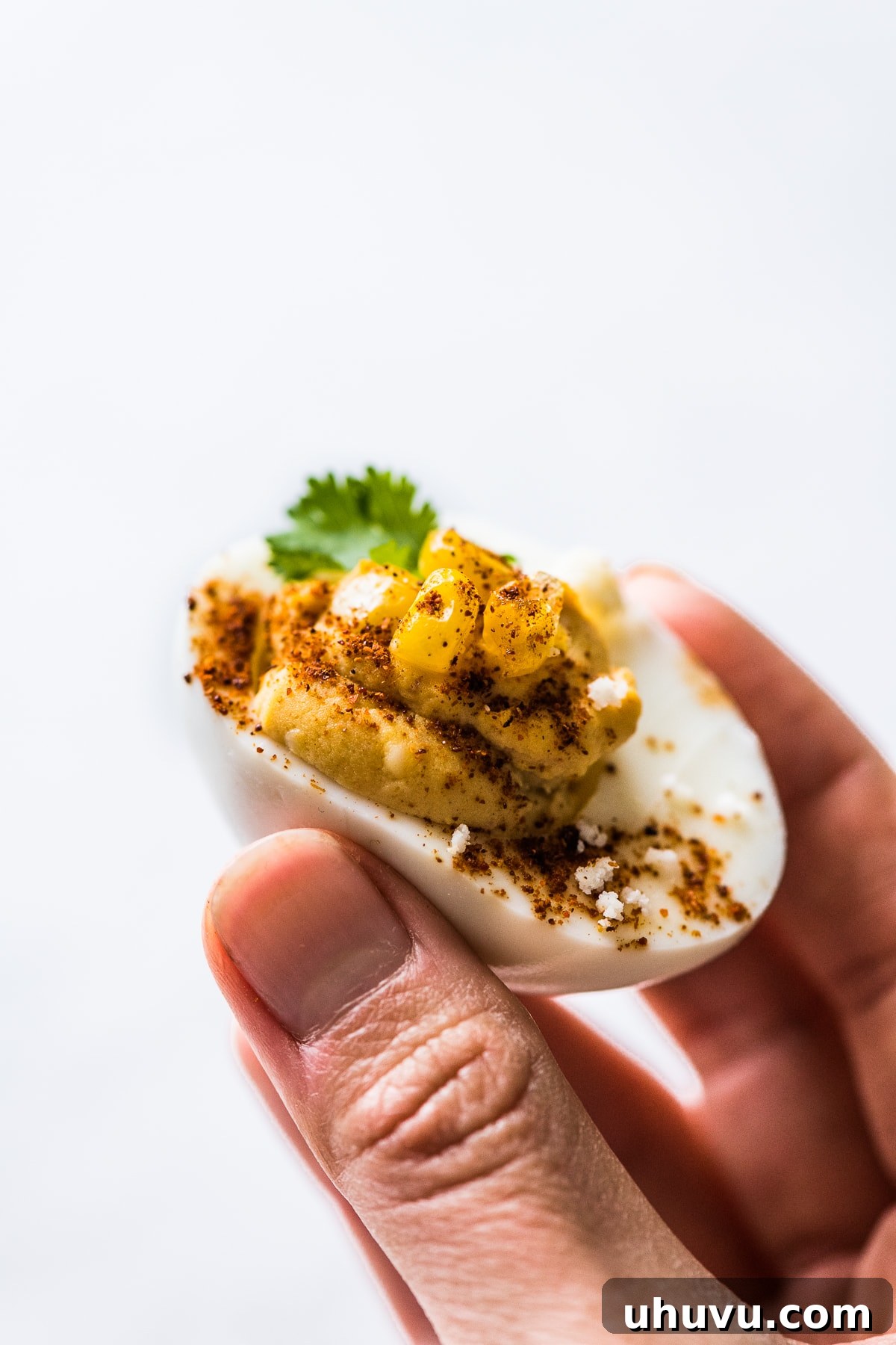 Elote Deviled Eggs 7 A hand gently holding a single, perfectly garnished Mexican street corn deviled egg, showcasing its appealing texture and vibrant colors.